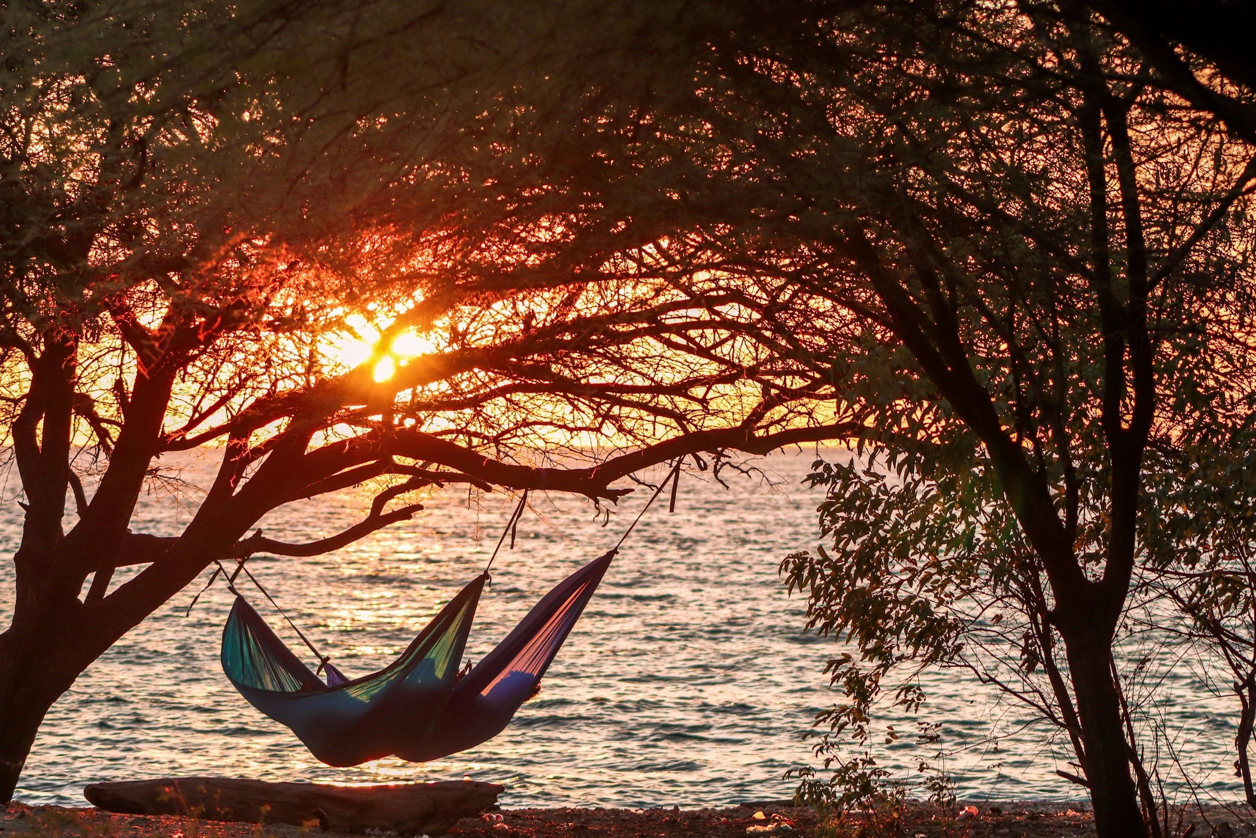 Two people in hammocks on the shore of a lake at sunset, illustrating time for rest and recovery