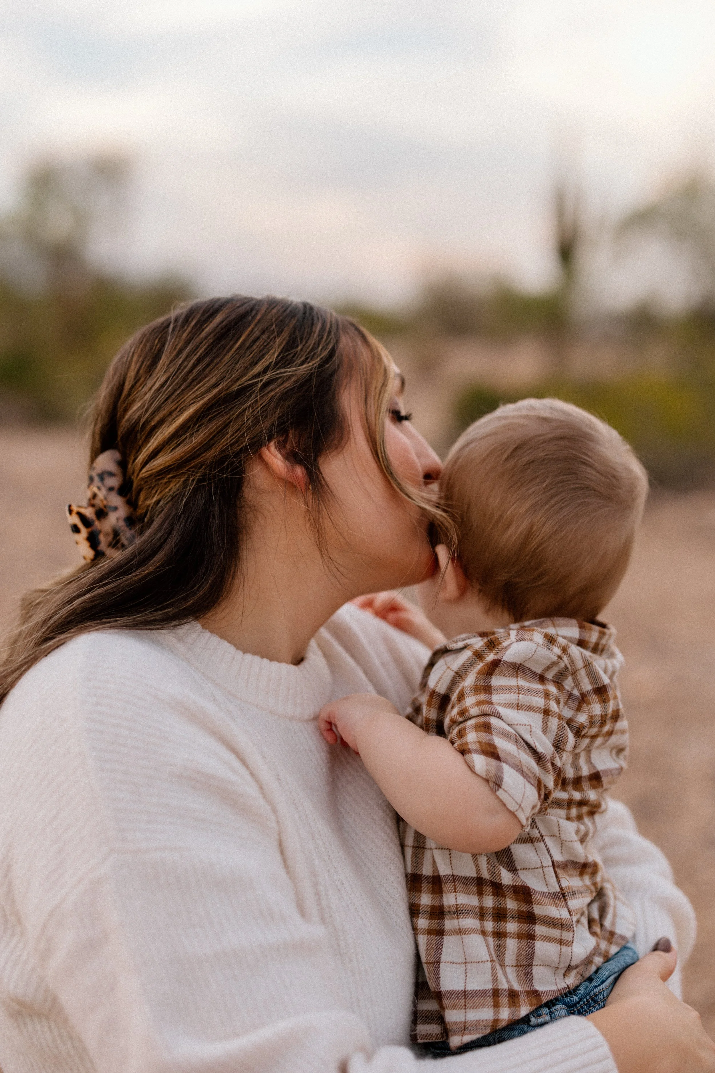 A woman holding a young boy outdoors, with their faces close together, during sunset.