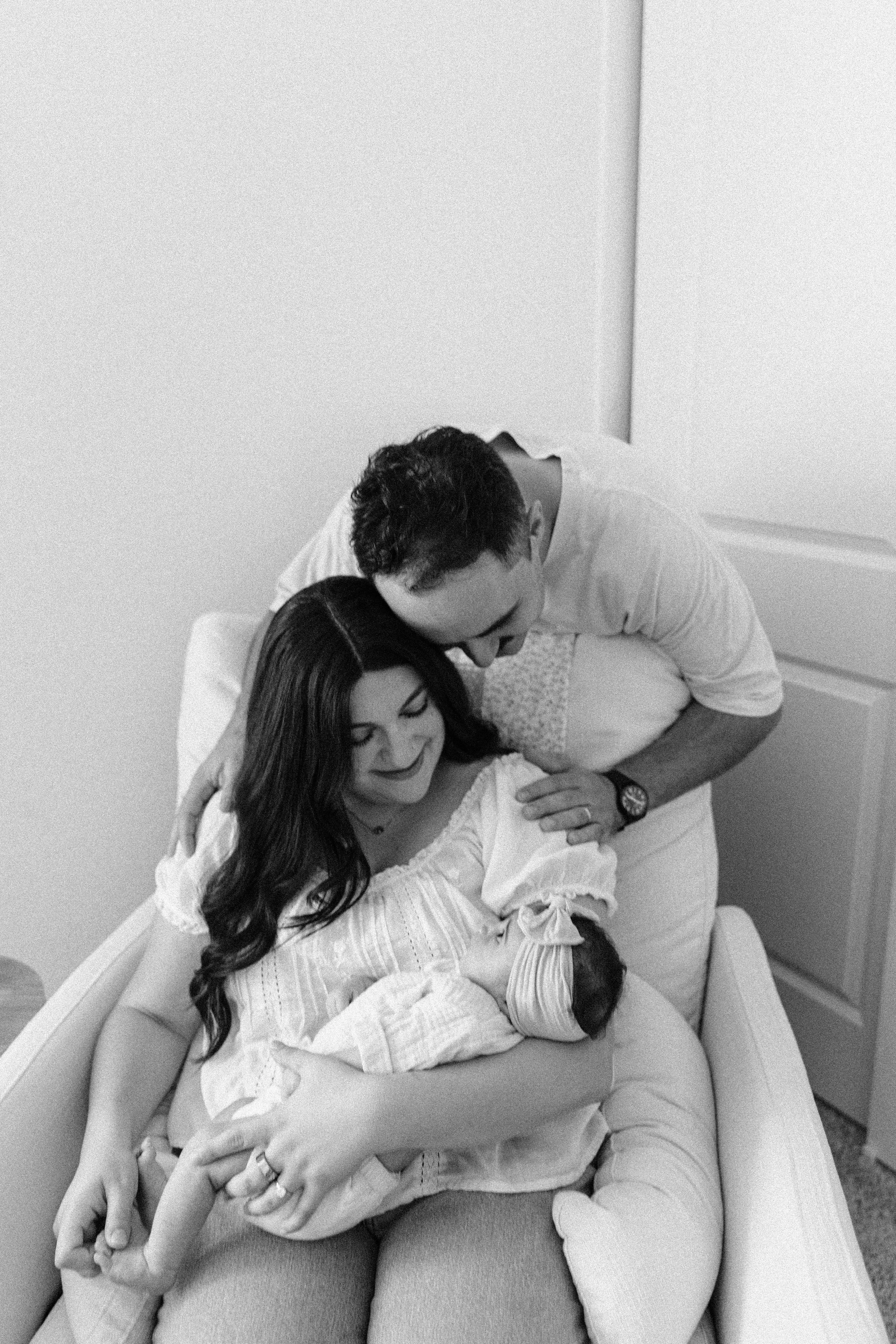 A woman holding a newborn baby, with a man leaning over her, in a hospital room.