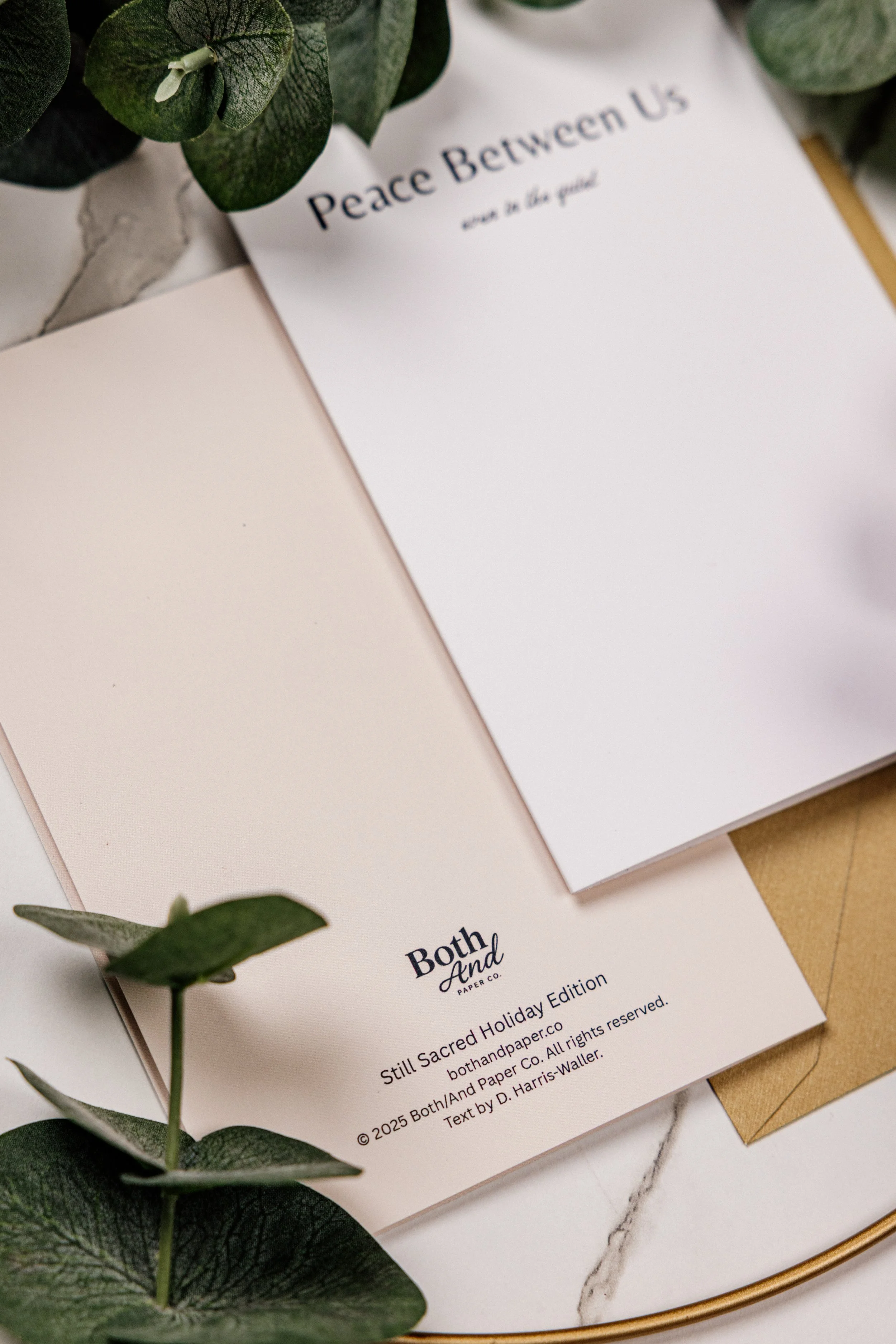 Open cards with printed text, surrounded by green leaves and a marble surface, on a gold tray.