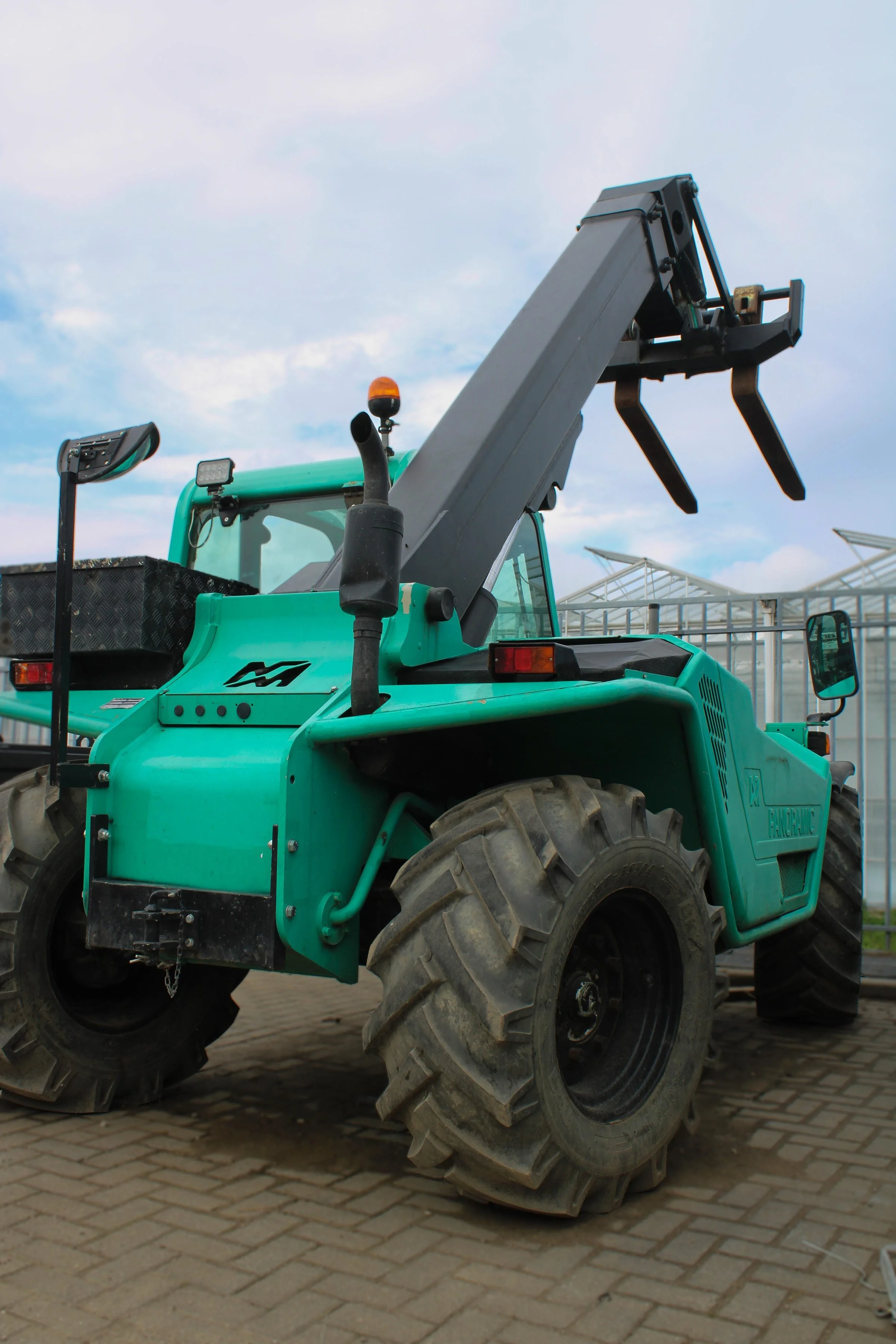 Groene landbouwtractor op een geplaveide ondergrond met een blauwe lucht en enkele glazen gebouwen op de achtergrond.
