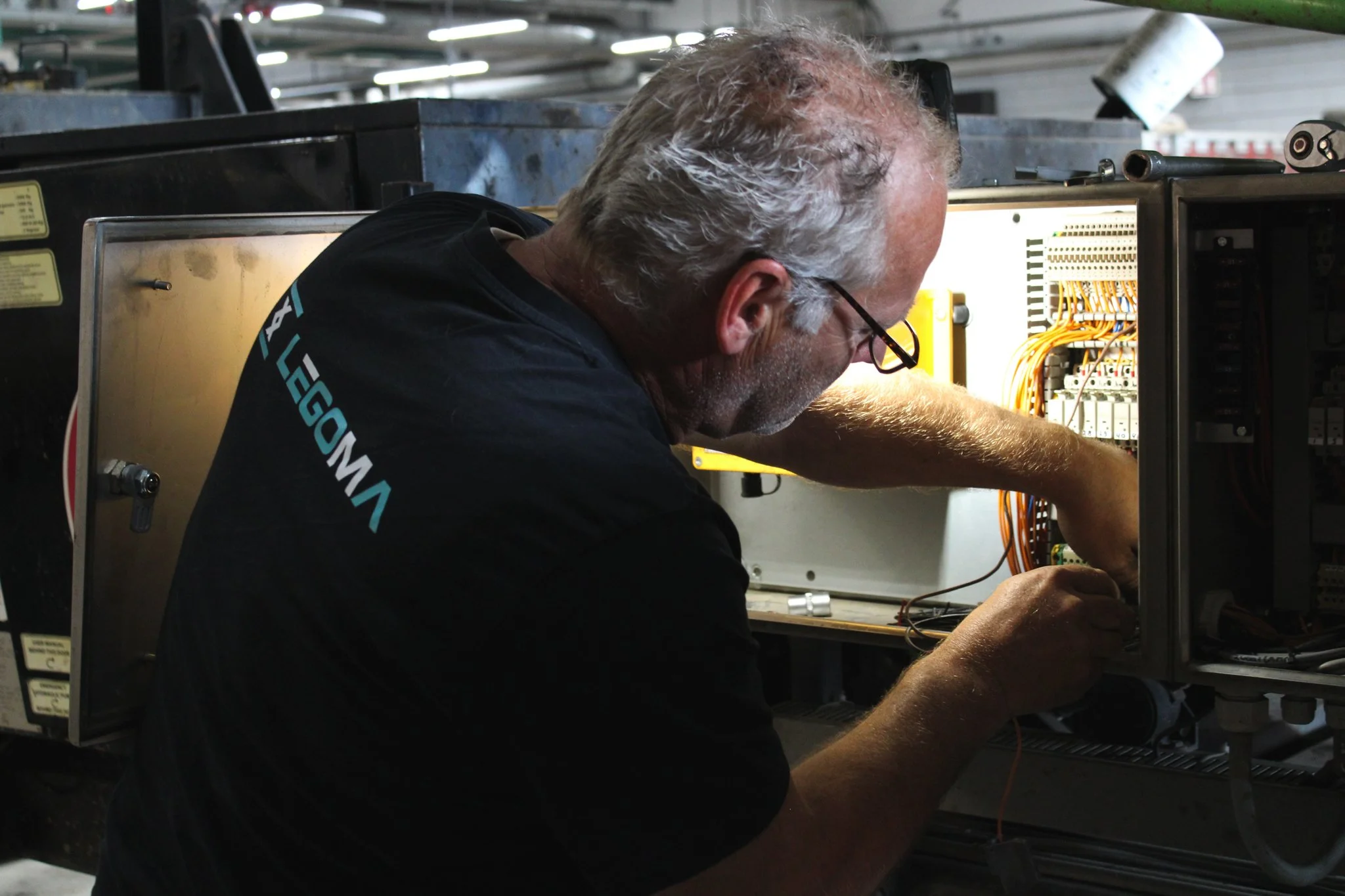 Man werkt aan een elektrisch paneel met draden in een industriële omgeving.
