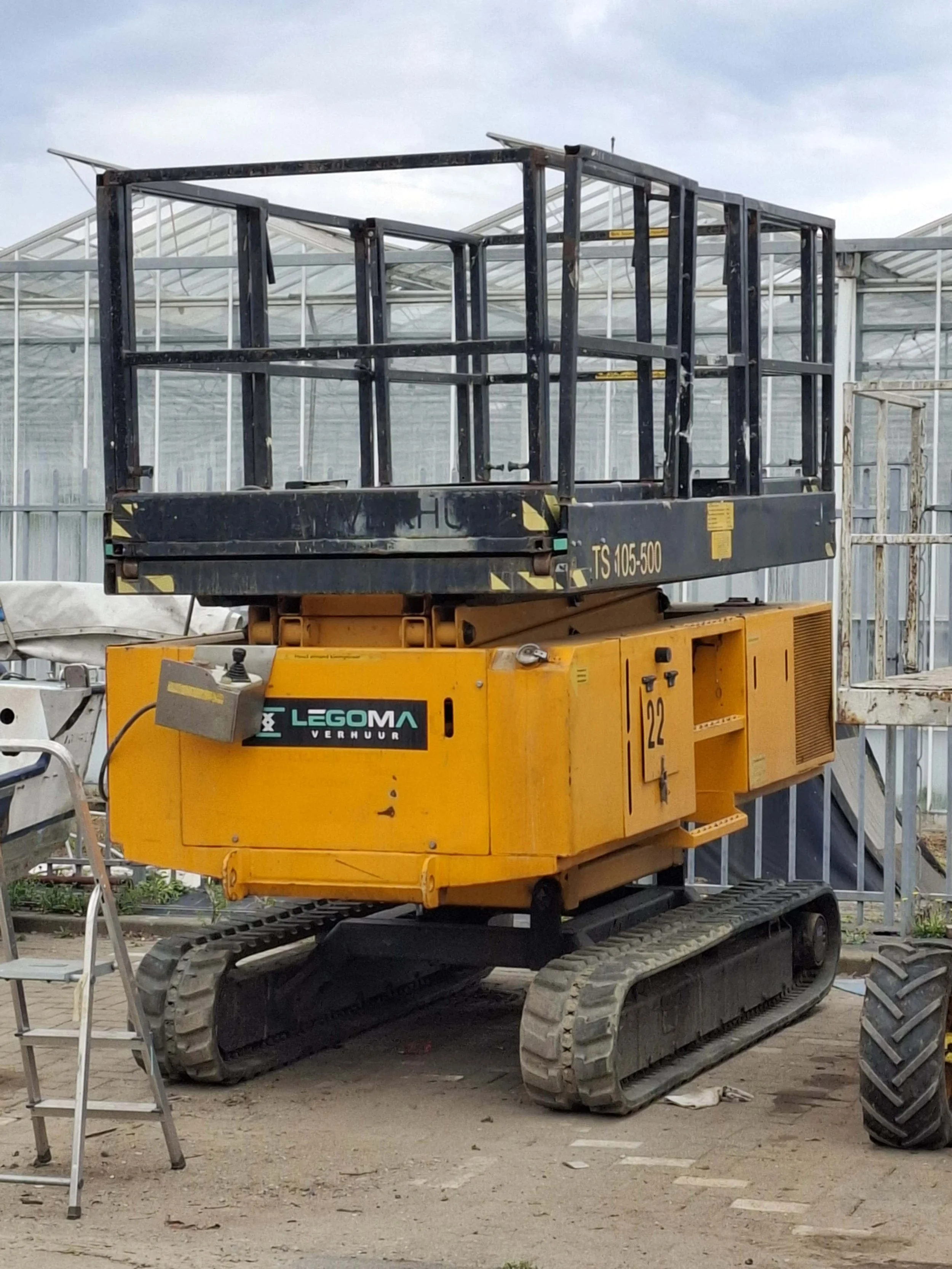 Bouwkraan met een zwarte platformschaal op een bouwplaats, met een metalen, gele basis en tracks.