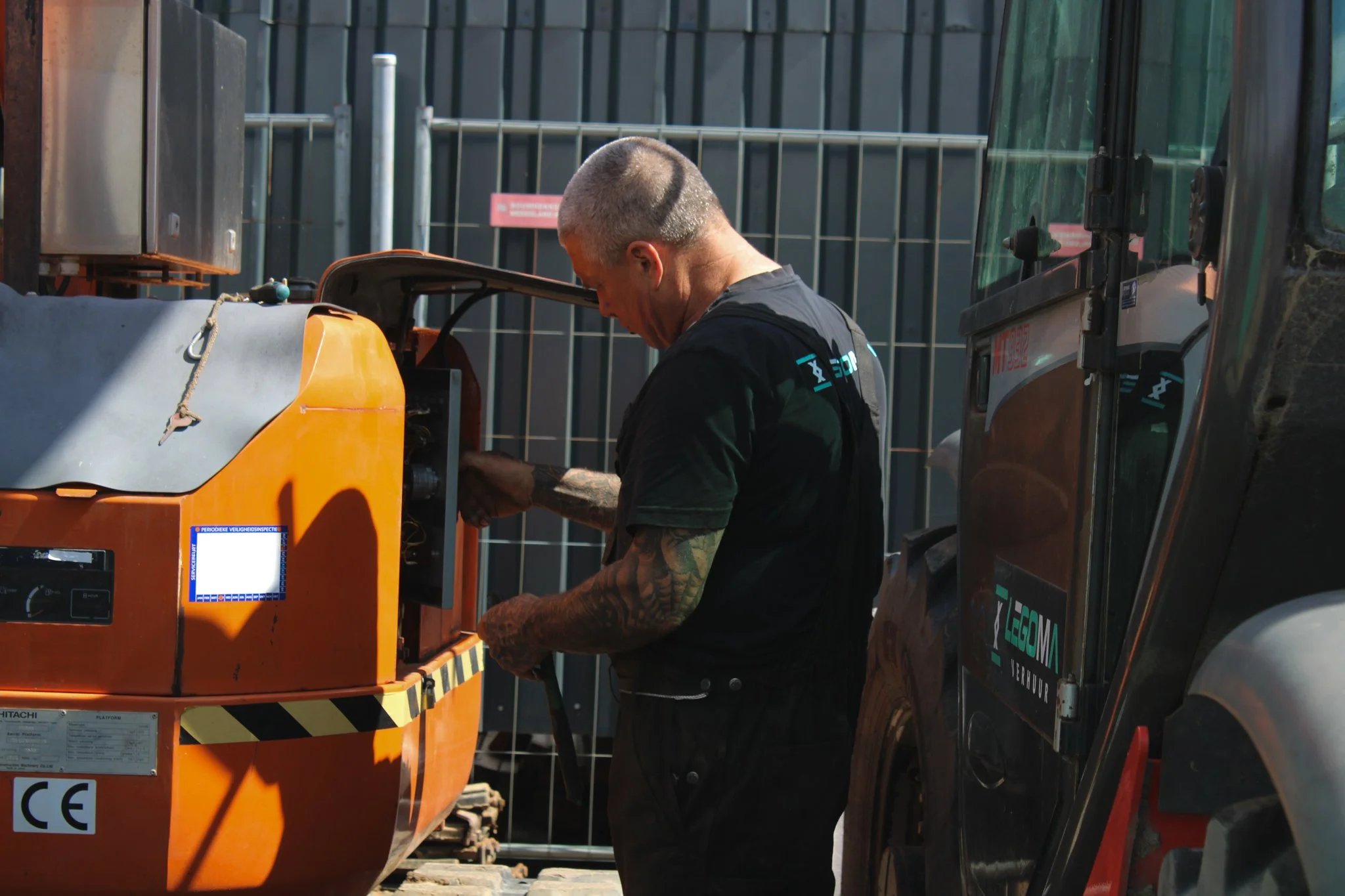 Man die onderhoud aan een grote orange bouwmachine.