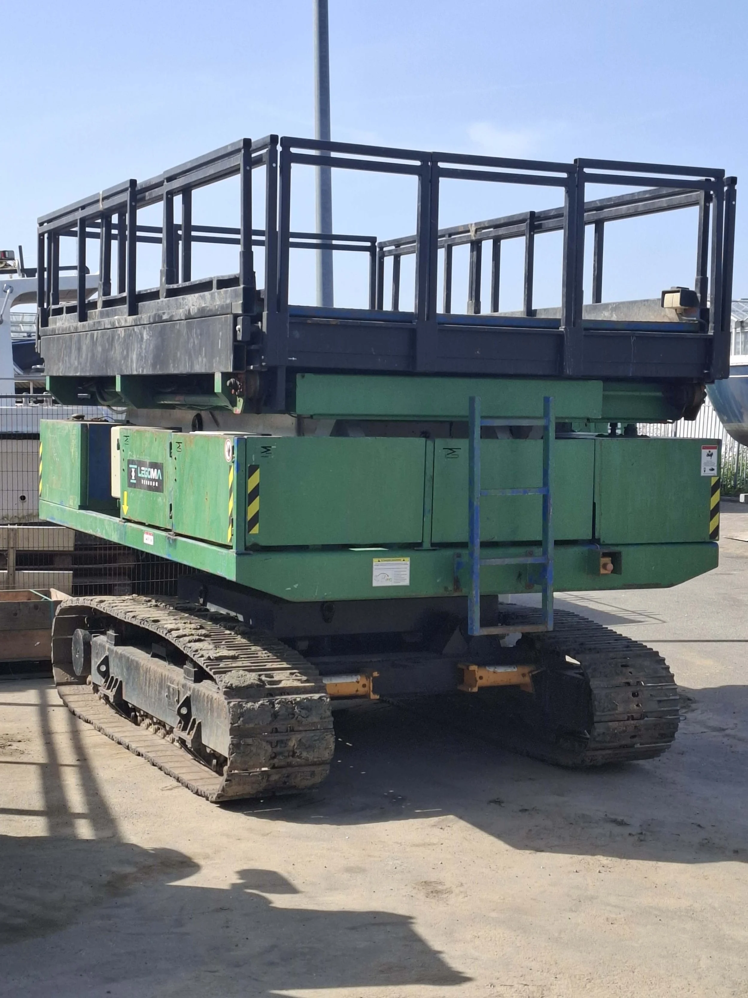 Een metalen steiger met traptreden op een bouwplaats, geplaatst op een rupsmachine op gravel.