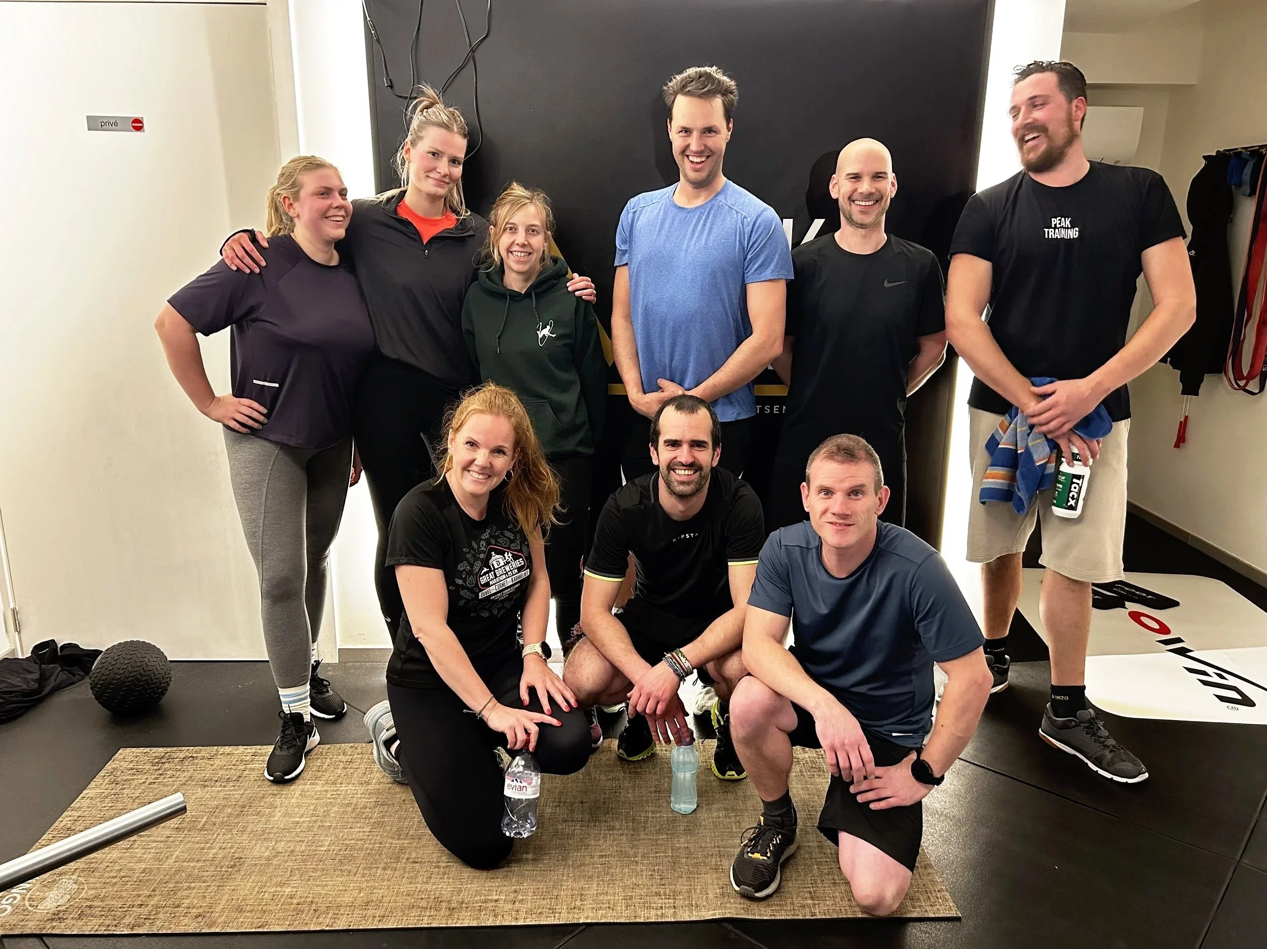 Group of nine people in a gym, smiling and posing for a photo, with exercise equipment around them.