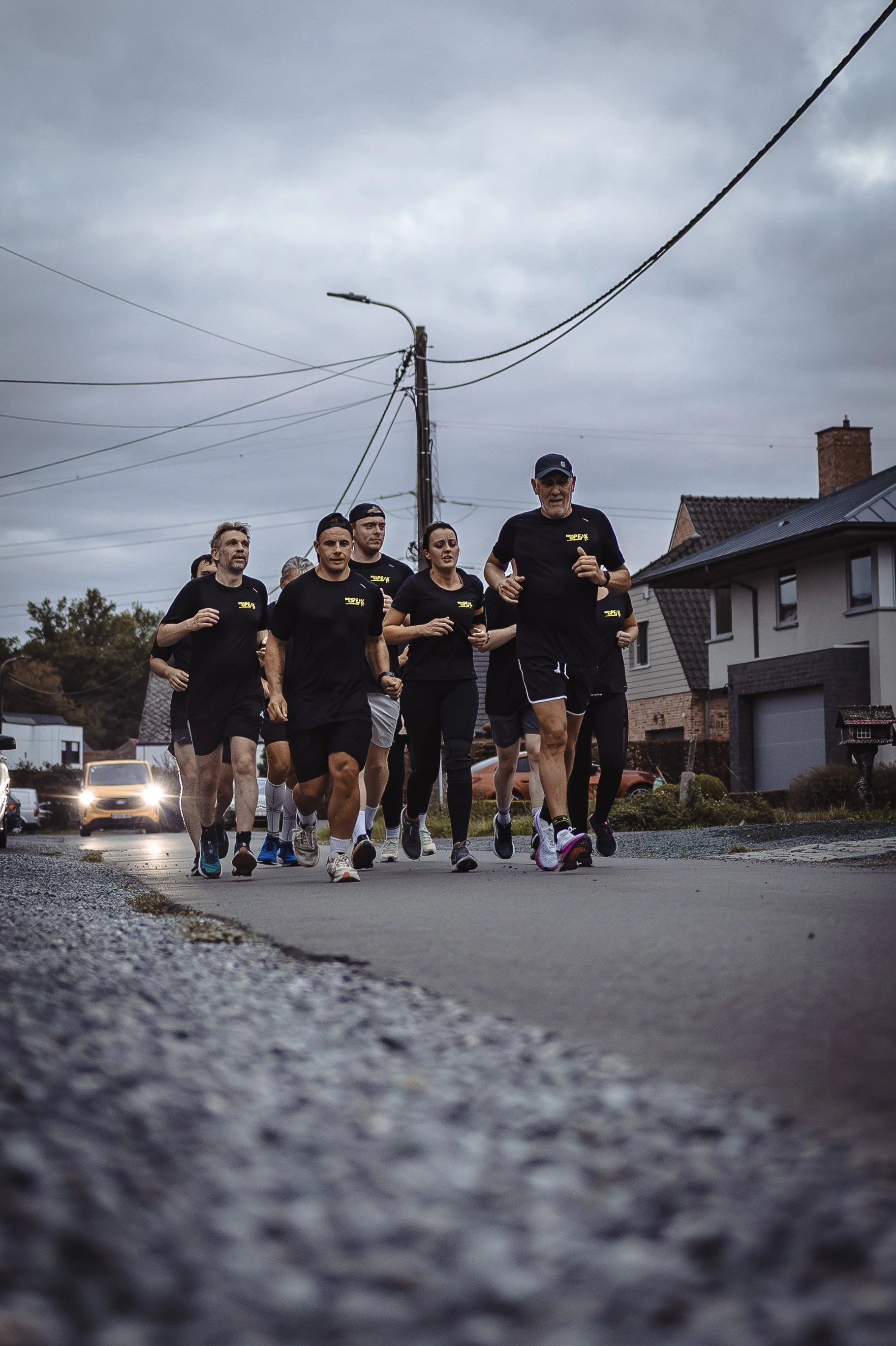 Een groep hardlopers loopt samen op een straat tijdens een training of race, onder een bewolkte hemel.