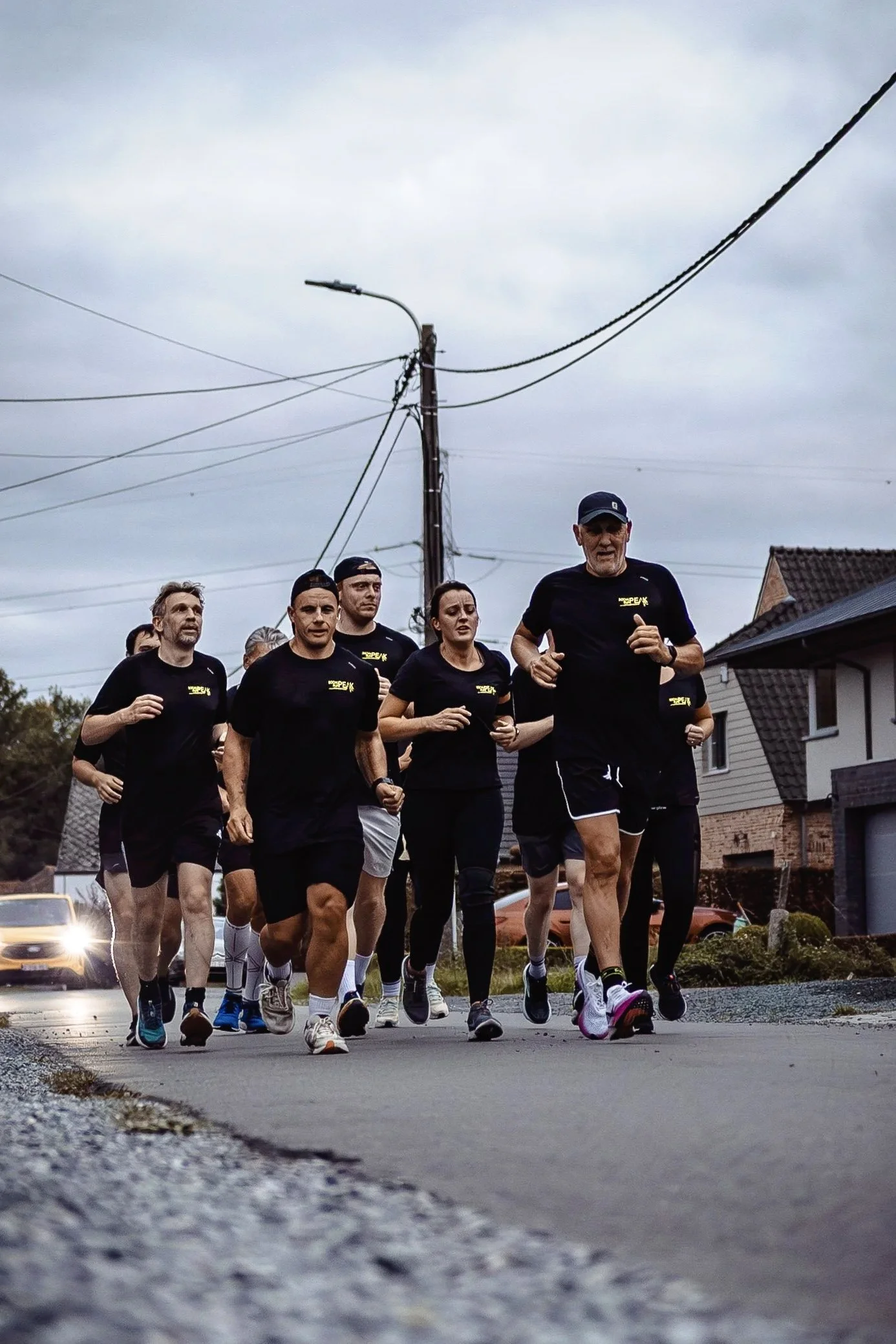 Group of people running together outdoors on a cloudy day, wearing black athletic shirts and shorts.