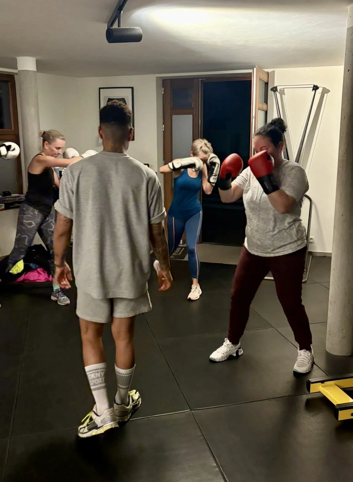 Mensen trainen in een fitnessruimte, met drie vrouwen en één man, die verschillende vecht- of bokstechnieken oefenen.