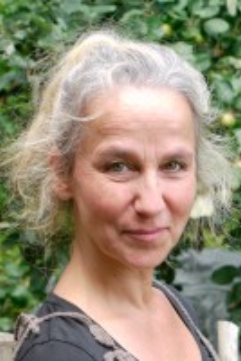 Petra Köhler - Dozentin der internationalen Schauspiel-Akademie für Film und Theater in Hamburg. Porträt einer älteren Frau mit grauem Haar vor grüner Natur.