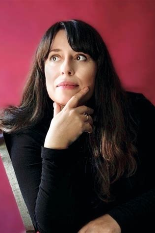 Veronique Elling - Dozentin der internationalen Schauspiel-Akademie für Film und Theater in Hamburg. Frau mit langem dunklem Haar, nachdenklich, berührt ihr Kinn, vor rosa Hintergrund