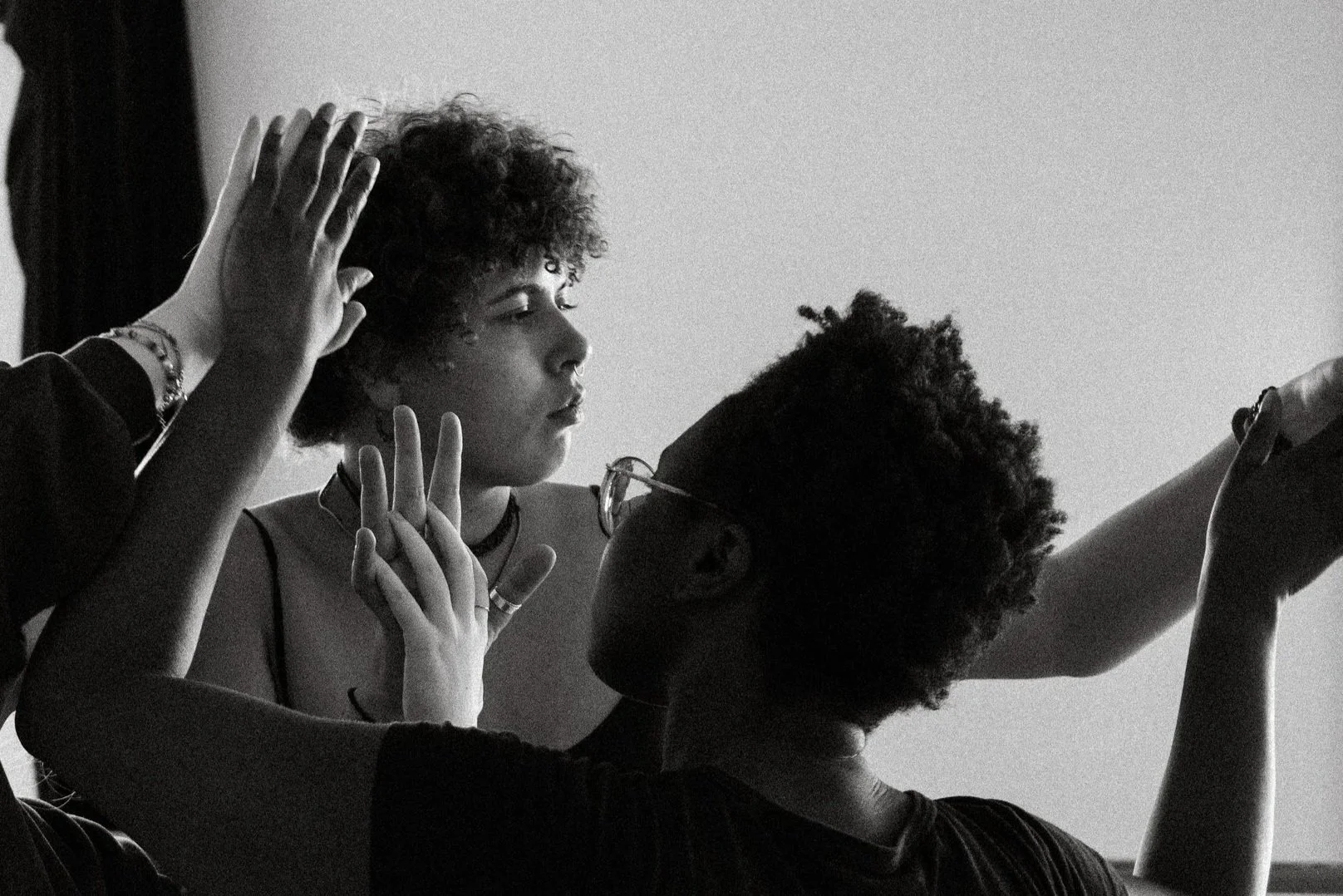 Drei Menschen mit dunklen Haaren und Brillen, die sich berühren und sich gegenseitig berühren, in einer intimen Atmosphäre, schwarz-weiß Fotografie.