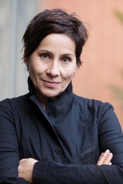 Annett Kruschke - Dozentin der internationalen Schauspiel-Akademie für Film und Theater in Hamburg. Eine Frau mit kurzen dunklen Haaren, trägt einen schwarzen, hohen Kragen und schaut in die Kamera.