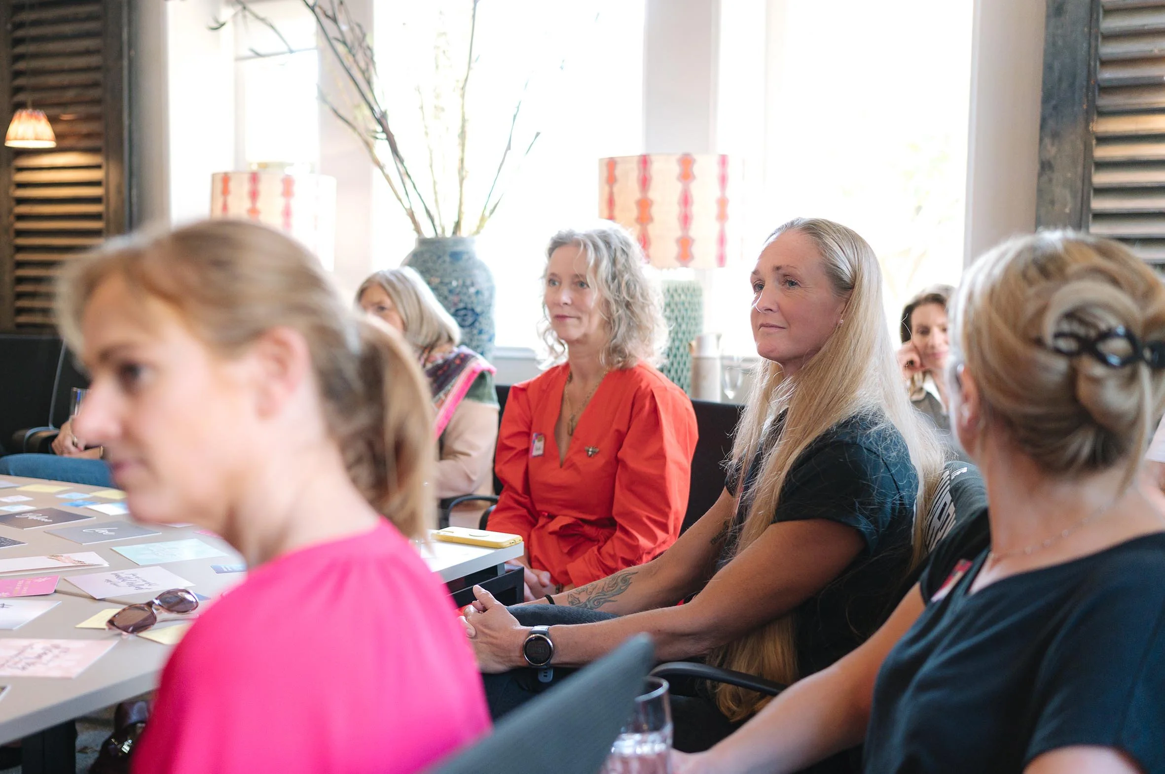 Group of women seated at a conference table attending a meeting or workshop with natural light coming through the windows.