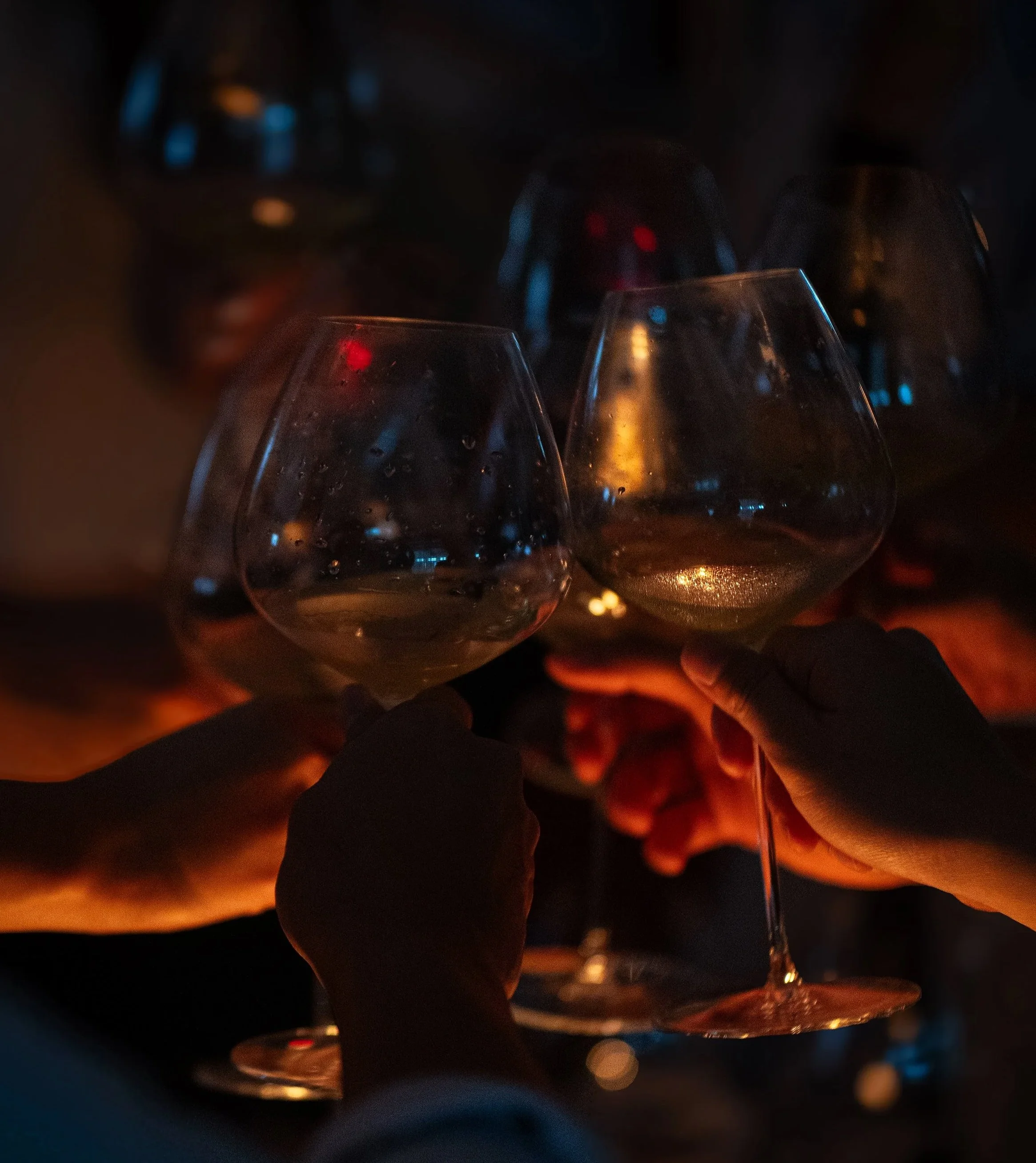 Group of people holding wine glasses together in a toast, dimly lit setting.
