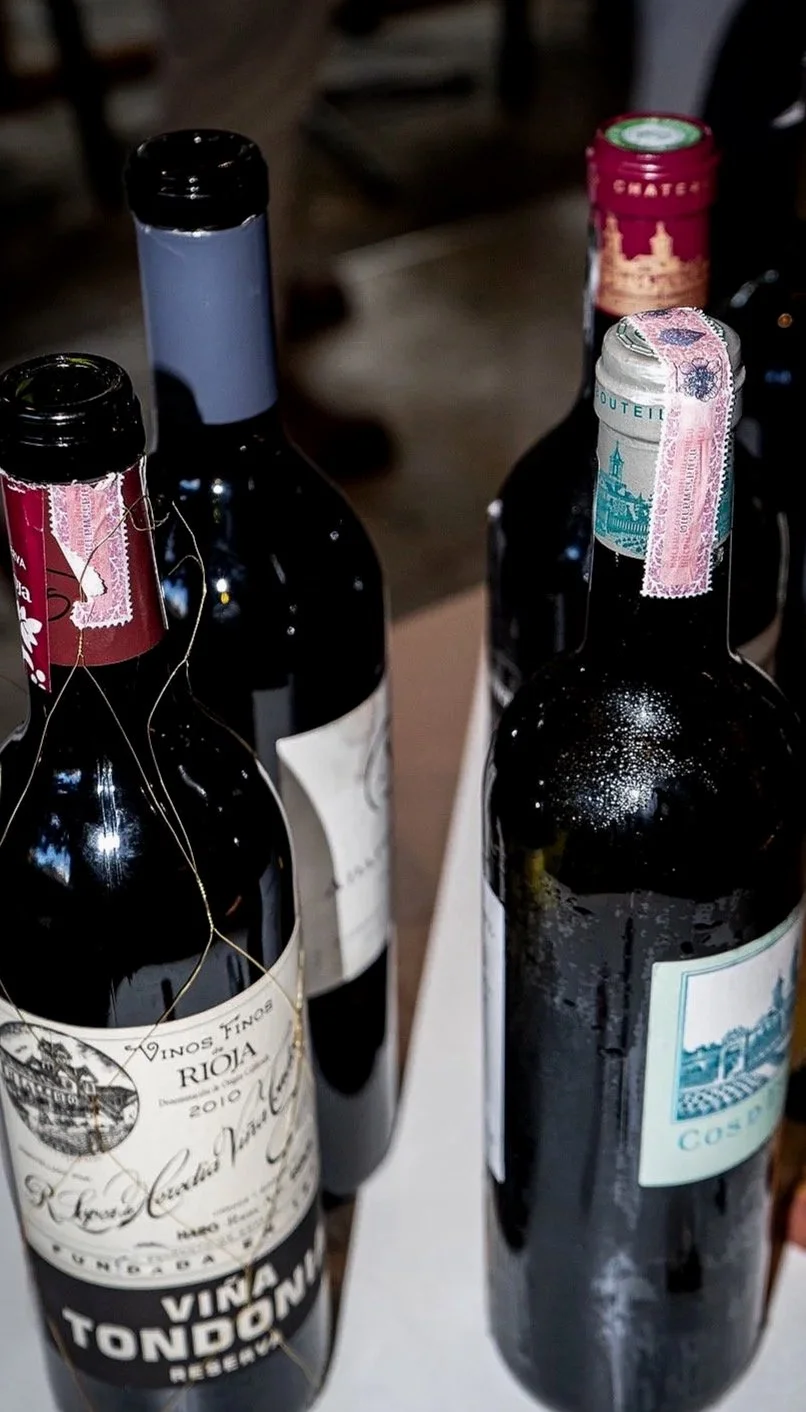 Several bottles of red wine, including Rioja and other labels, on a white surface in a dimly lit setting.