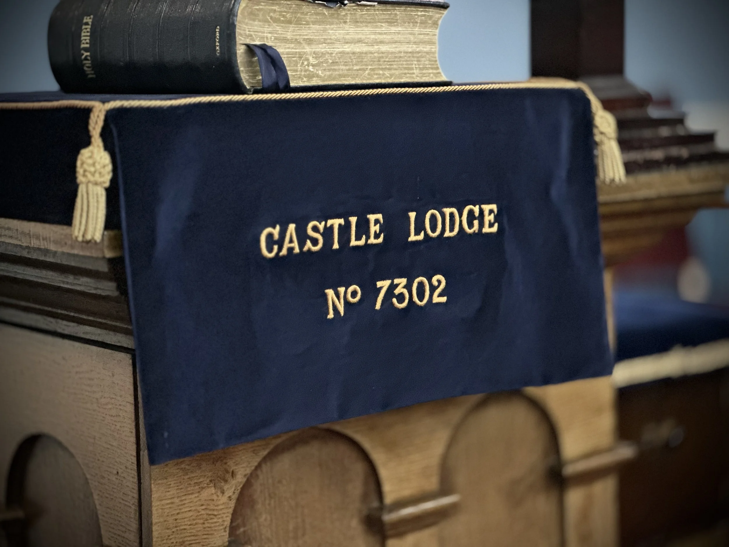 Close-up of a blue velvet cloth with gold embroidery that reads 'CASTLE LODGE No 7302,' draped over a wooden piece of furniture.