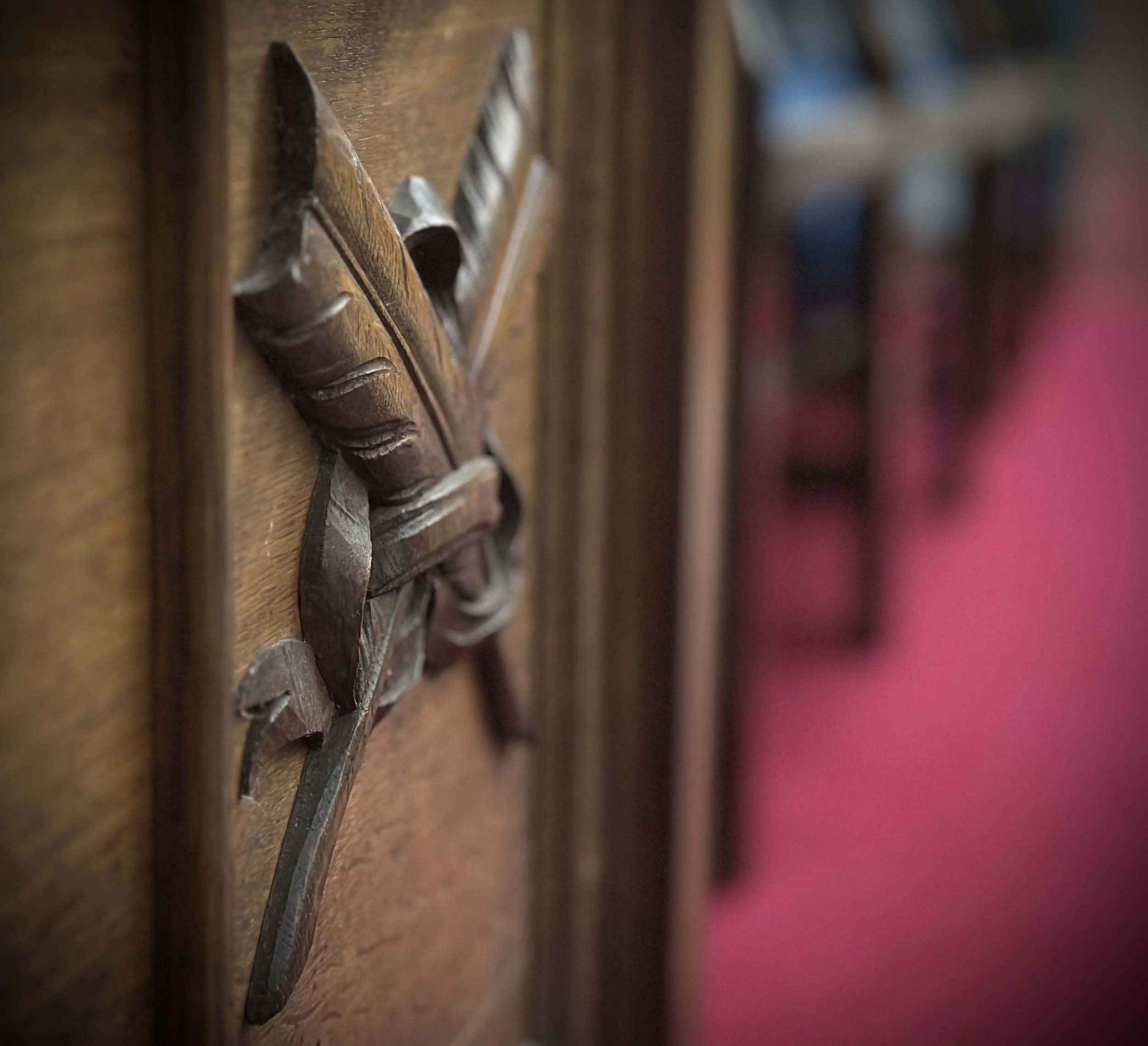 Close-up of a wooden carved decorative arrow with a ribbon tied around it, mounted on a wooden surface, with blurred background.