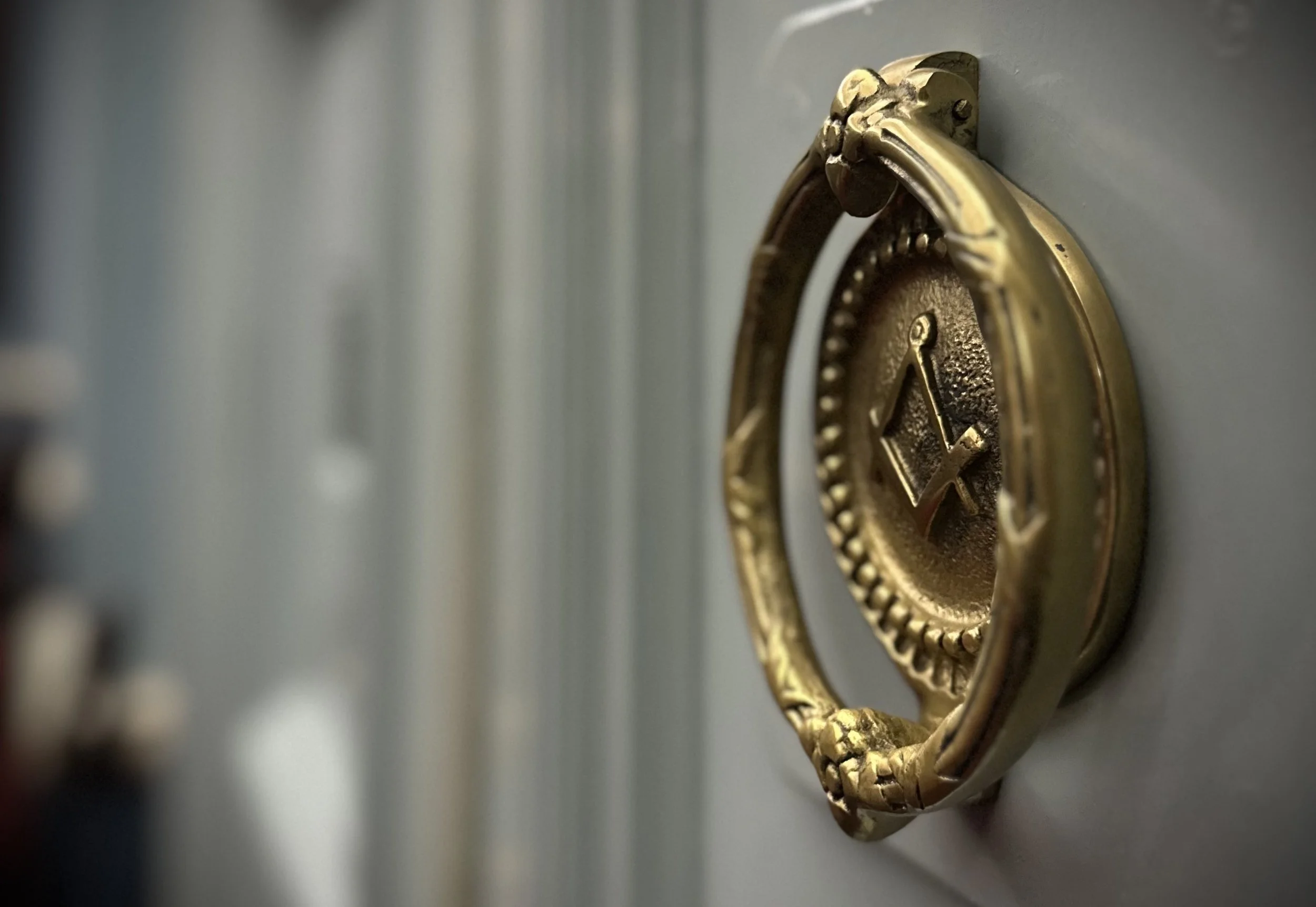 Close-up of a masonic door knocker mounted on a gray door.