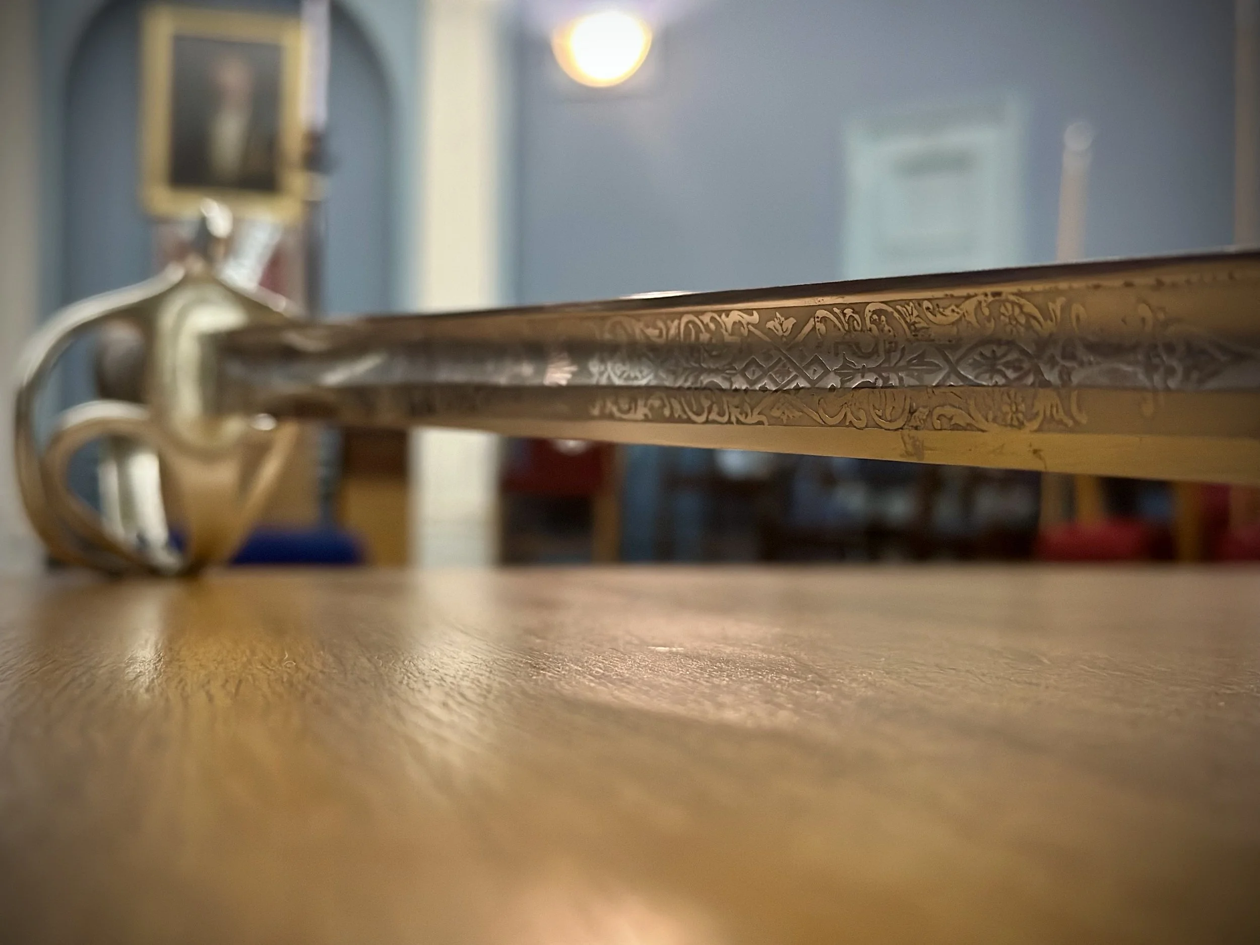 Close-up of a decorative sword with engraved details, resting on a wooden table.