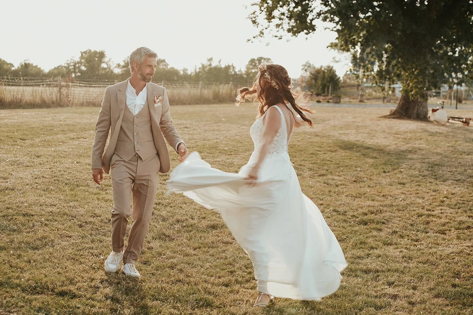 Un homme et une femme en robe de mariée dansant dans un champ en plein air, au coucher du soleil.