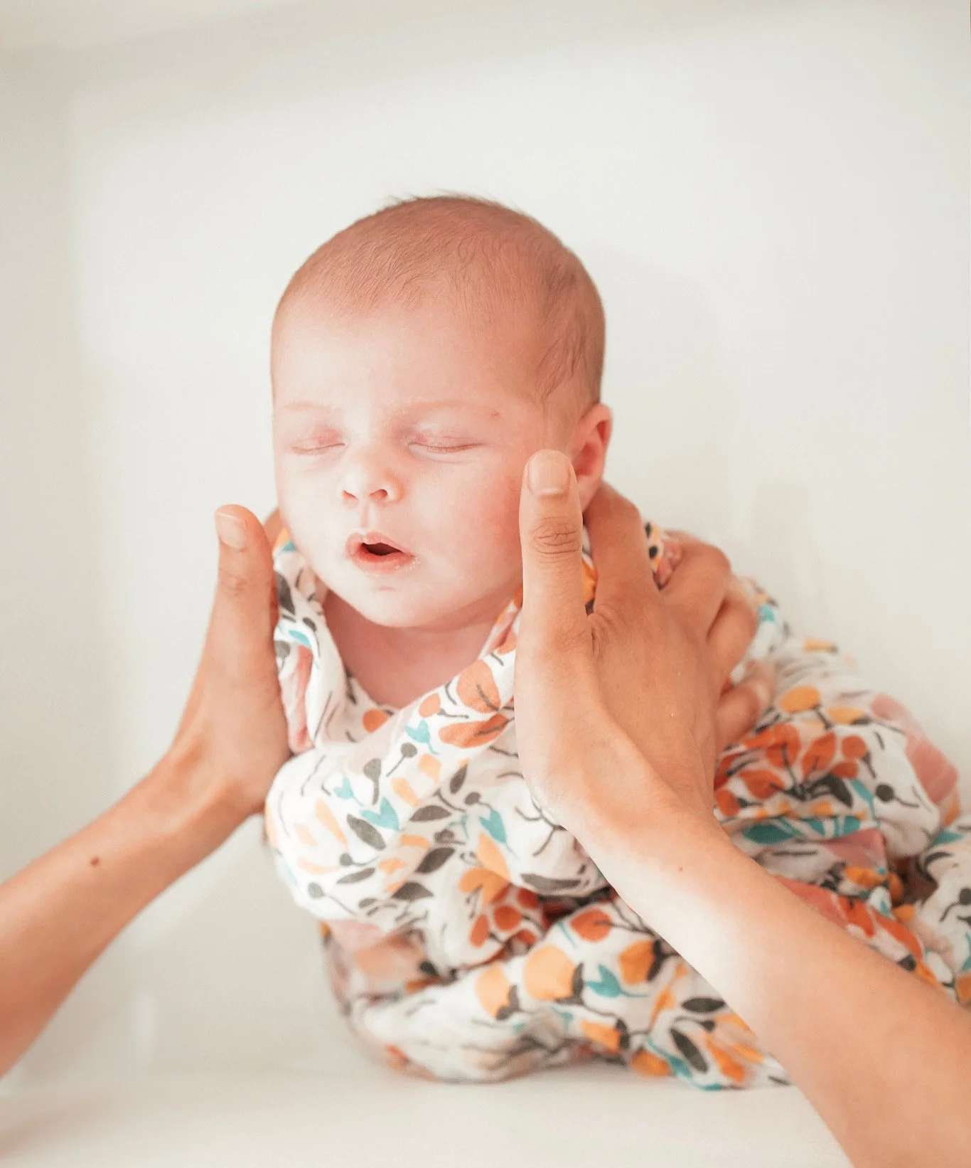 Un bébé endormi, tenu doucement par deux personnes, avec un fond clair.