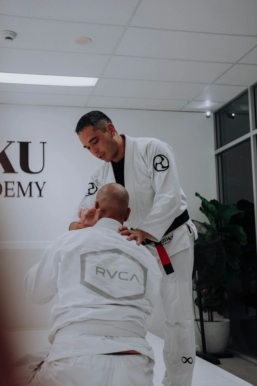 Kazoku Jiu Jitsu Academy black belt coach guiding a student through a technique during a white-gi class in Varsity Lakes