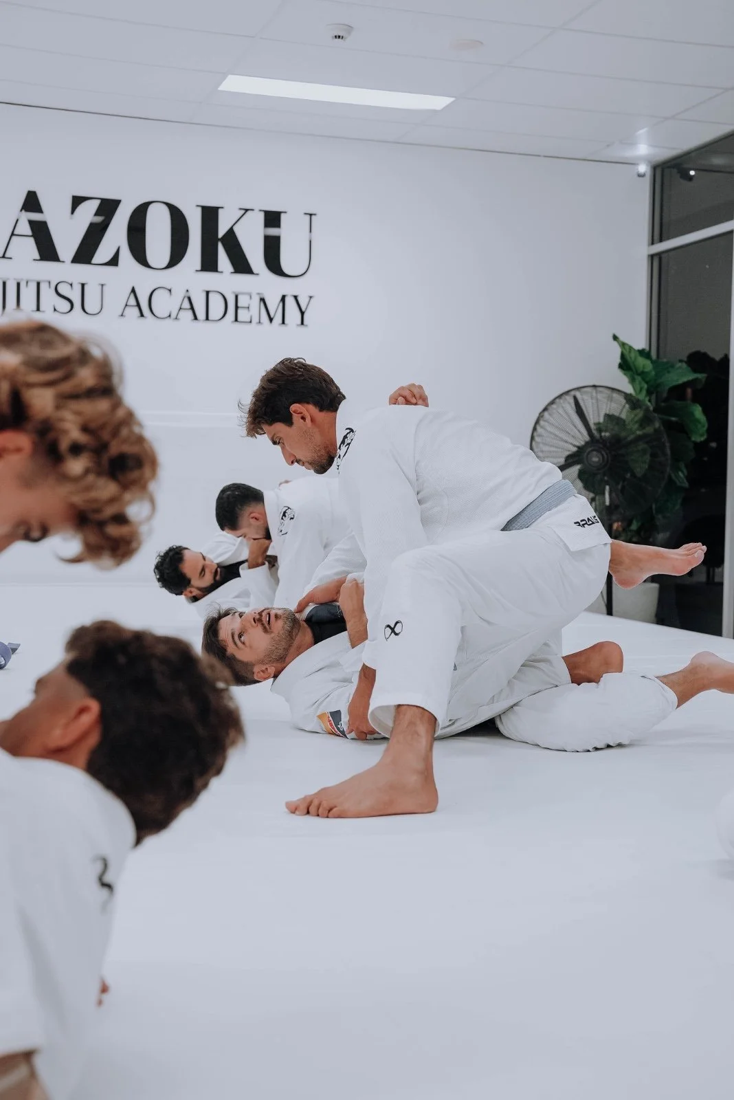 Students training Brazilian Jiu-Jitsu together on the mats at Kazoku Jiu Jitsu Academy in Varsity Lakes