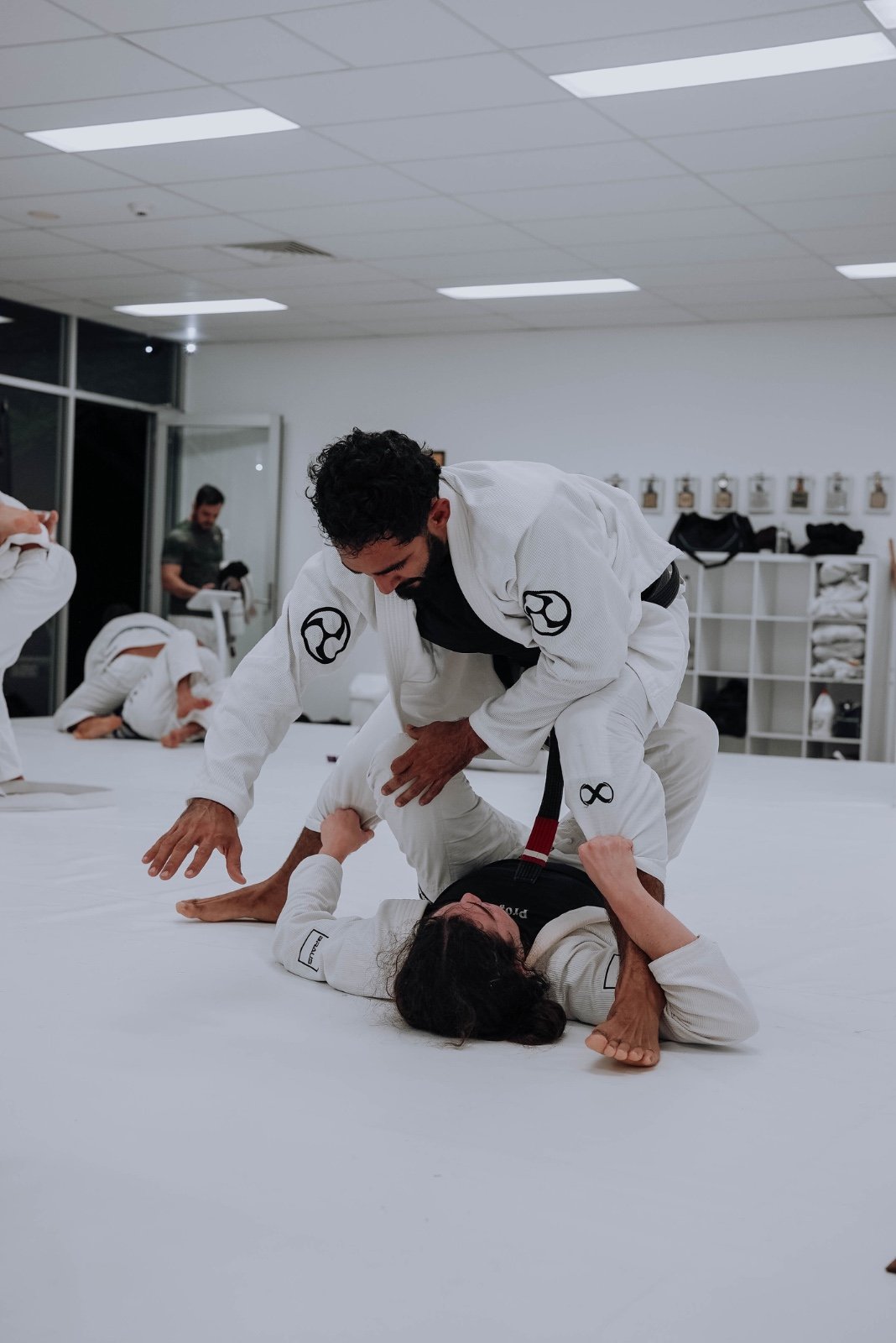 Two students in white gis sparring Brazilian jiu-jitsu on the mats at Kazoku Jiu Jitsu Academy in Varsity Lakes
