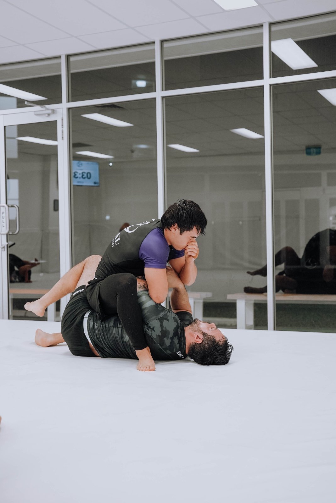 Two students rolling No-Gi in rash guards during a Brazilian jiu-jitsu class at Kazoku Jiu Jitsu Academy in Varsity Lakes