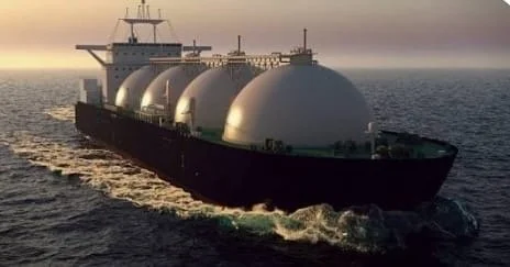 Large cargo ship carrying spherical tanks sailing on the ocean at sunset.