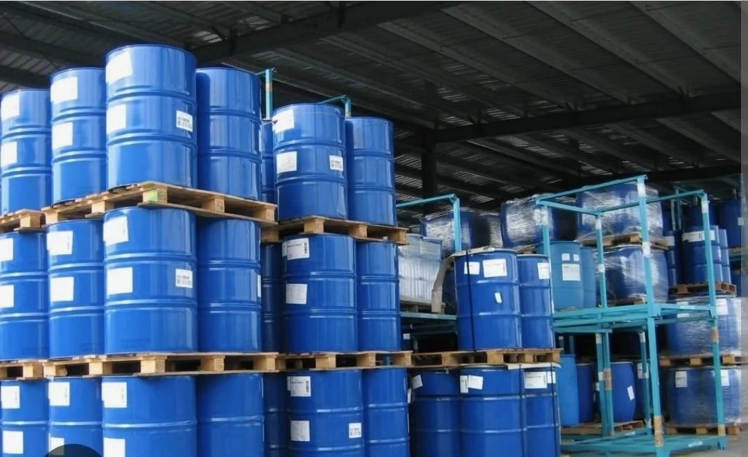 Stacks of blue industrial barrels stored on wooden pallets and metal racks in a warehouse.