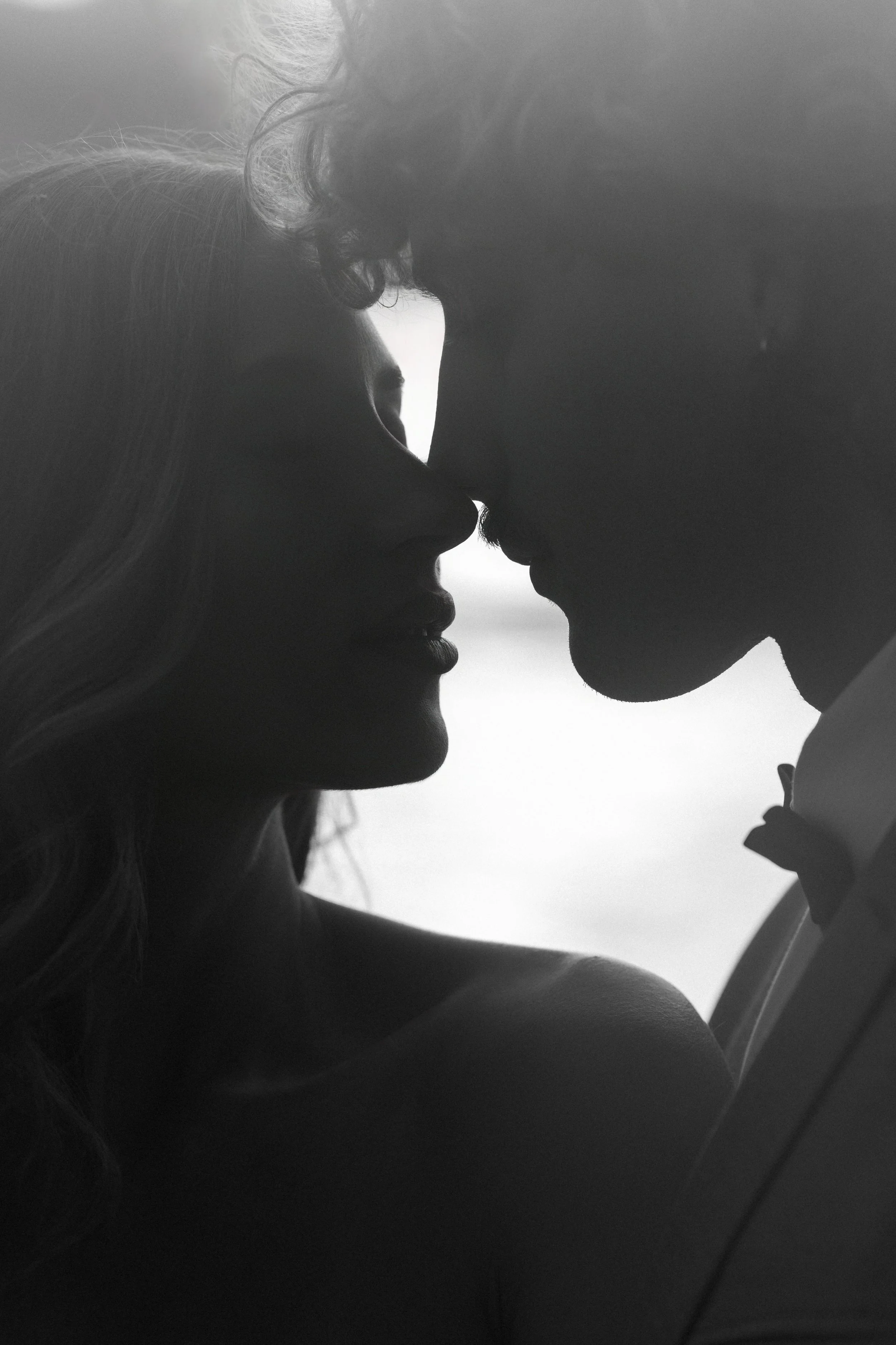 Silhouettes of a man and woman close together, about to kiss, against a light background, black and white photo.