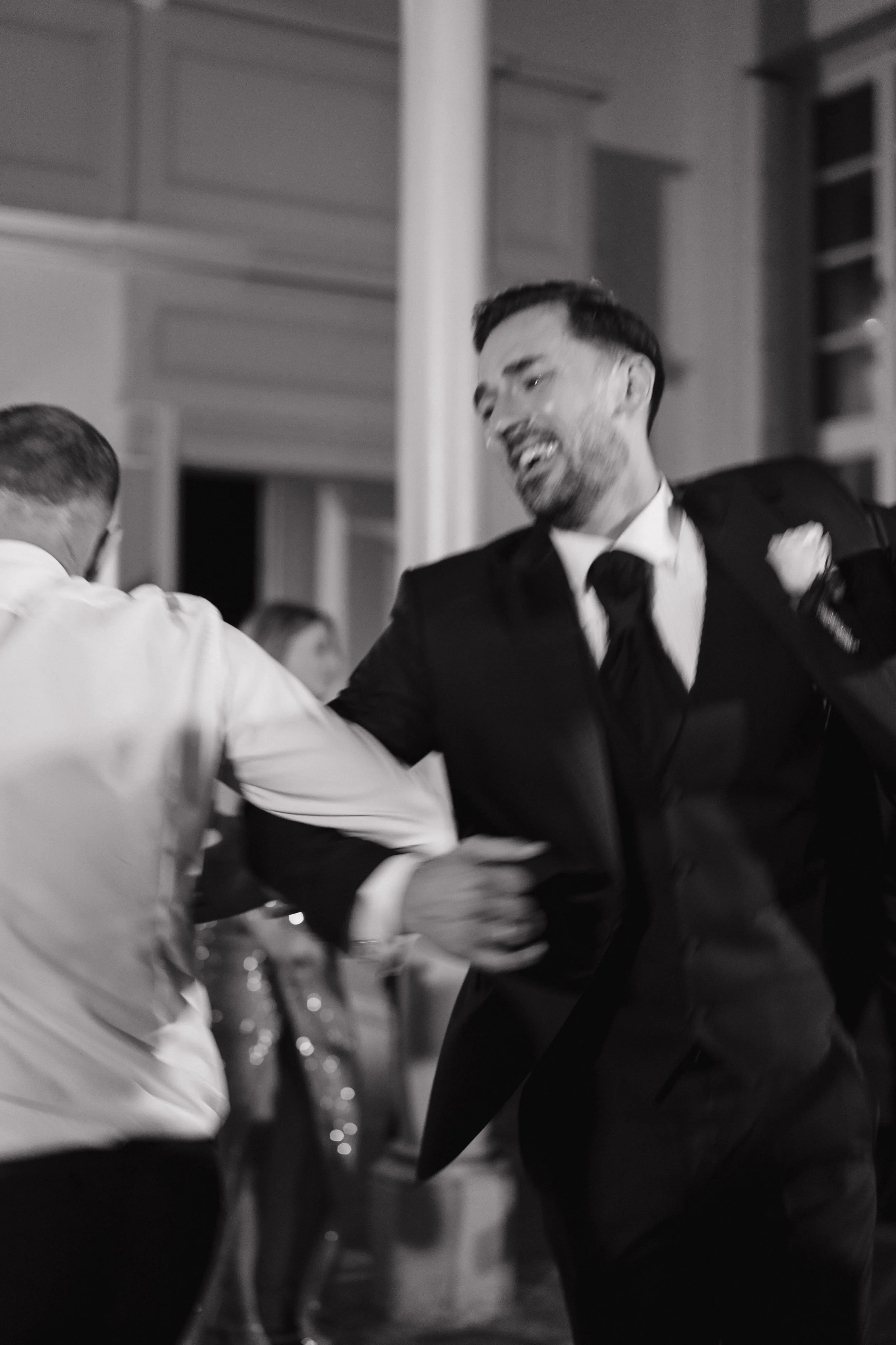 Two men dancing and smiling with a joyful expression in a formal setting, black-and-white photo.