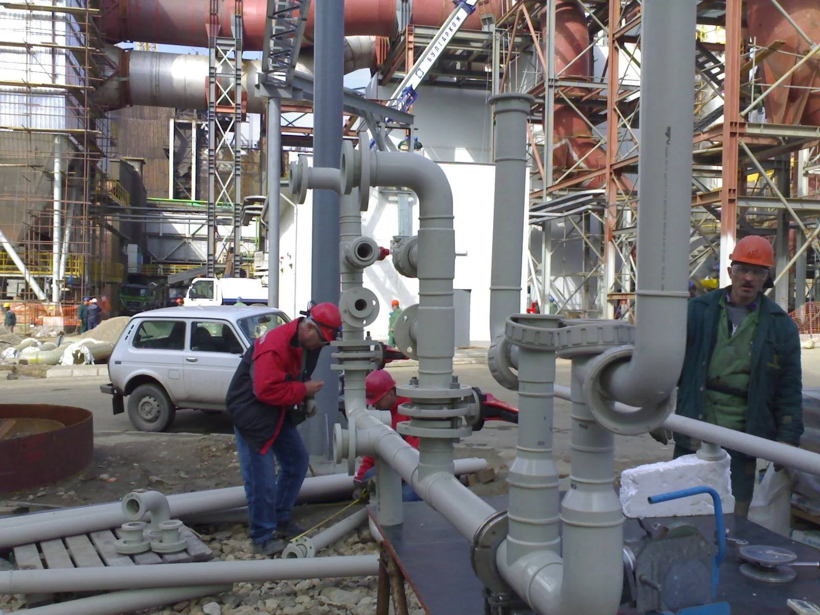 Construction workers wearing safety helmets working on pipes at an industrial construction site.