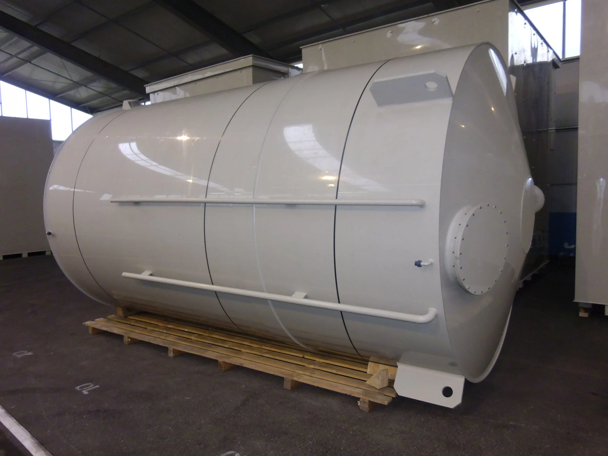 Large white industrial tank or vessel with a cylindrical shape and rounded ends, resting on a wooden pallet inside a warehouse.
