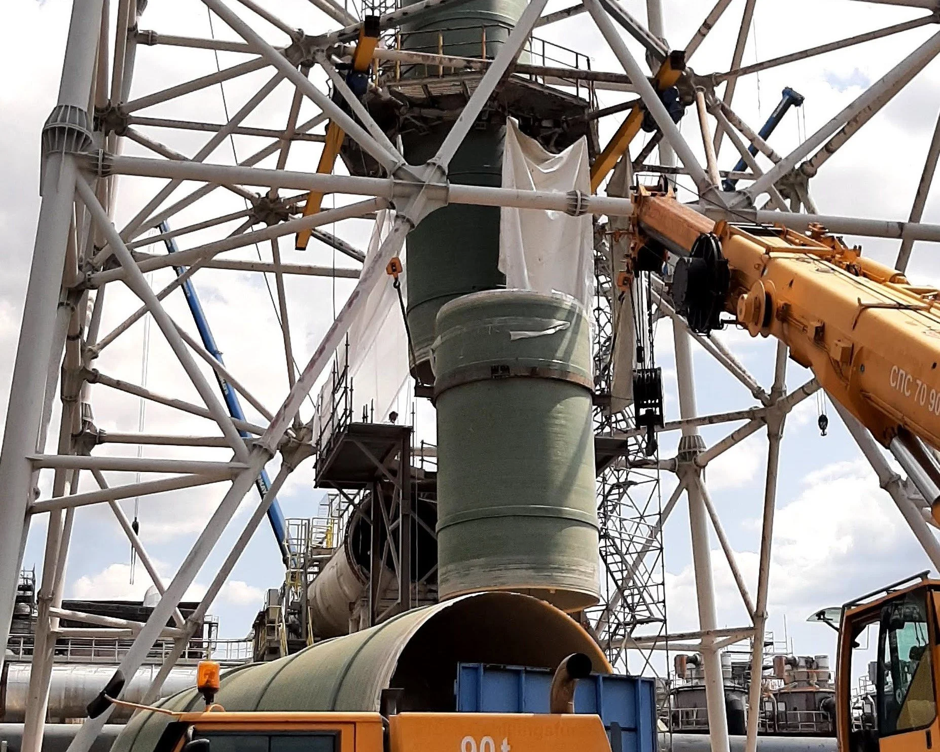Construction workers and machinery installing large structural components on a tall industrial lattice framework, possibly part of a construction or maintenance project.