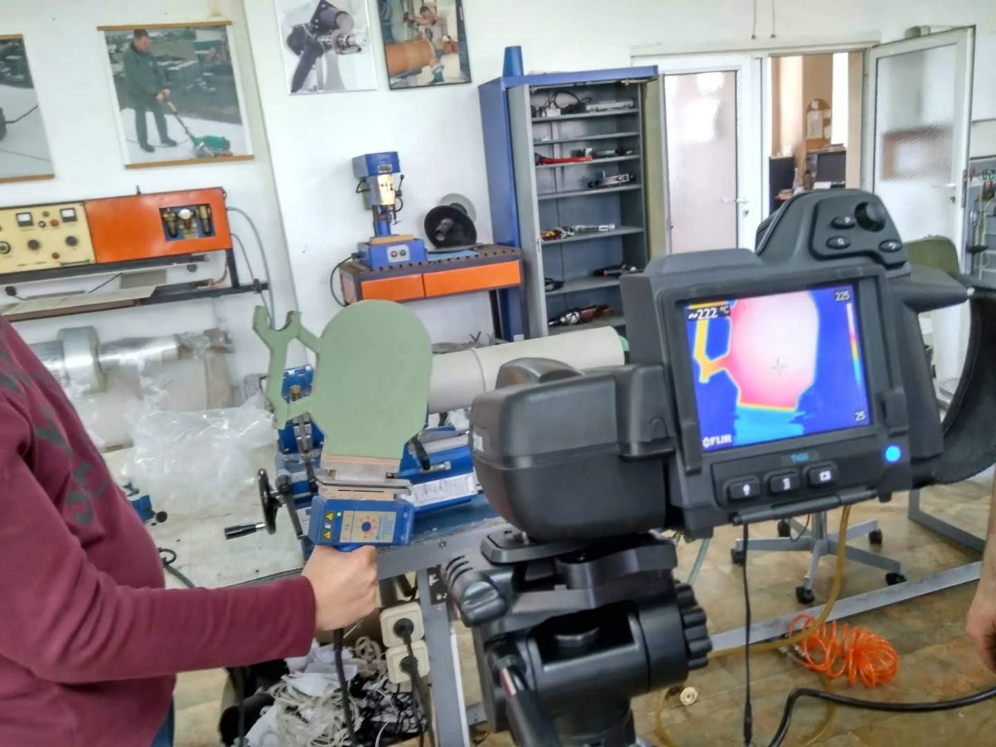 Camera recording a thermal image of a green object held by a person in a workshop.
