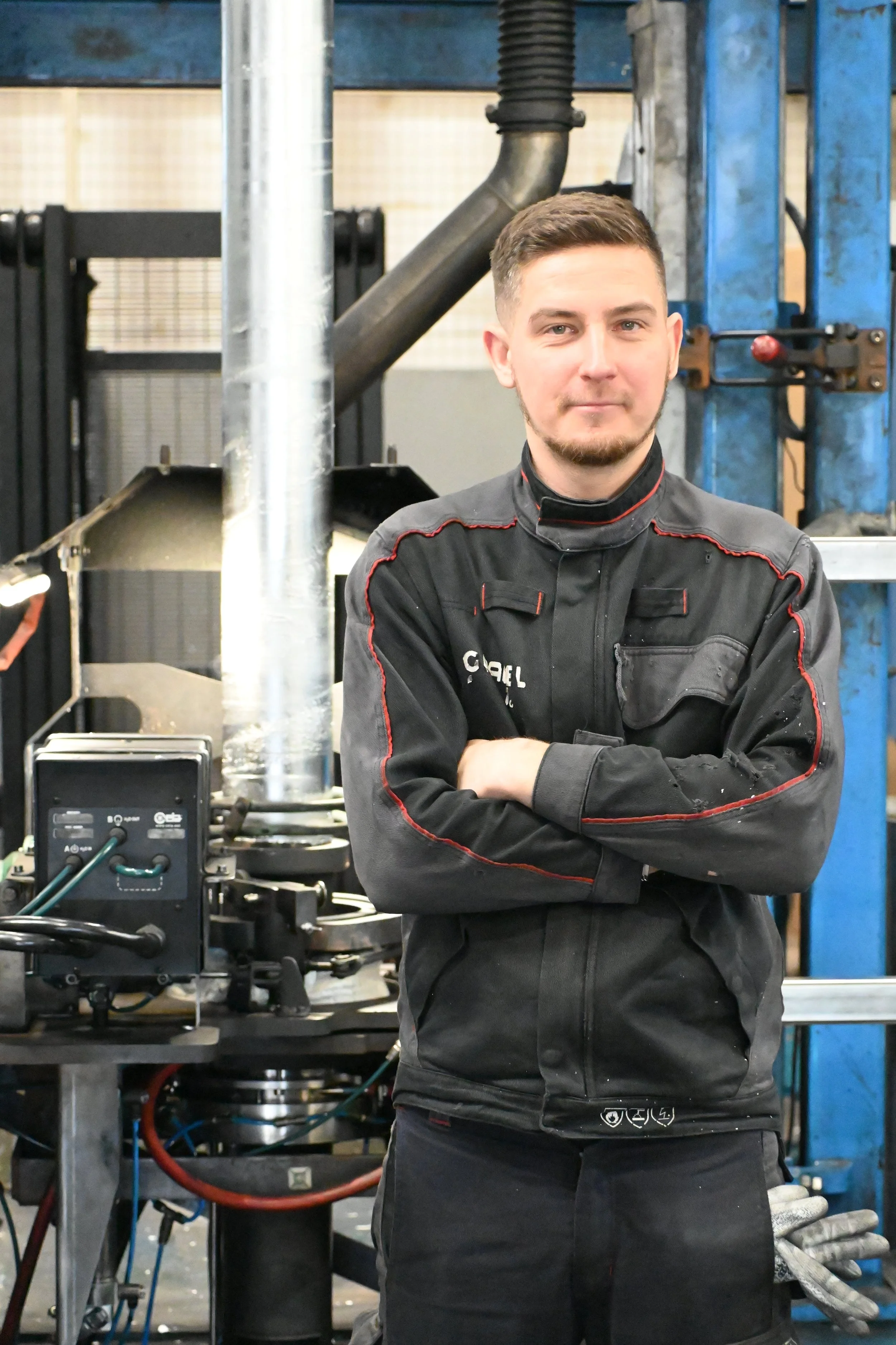 A man with glasses and a beard stands in front of industrial equipment, wearing a navy blue sweatshirt with the logo and text 'GRADEL' on the chest.