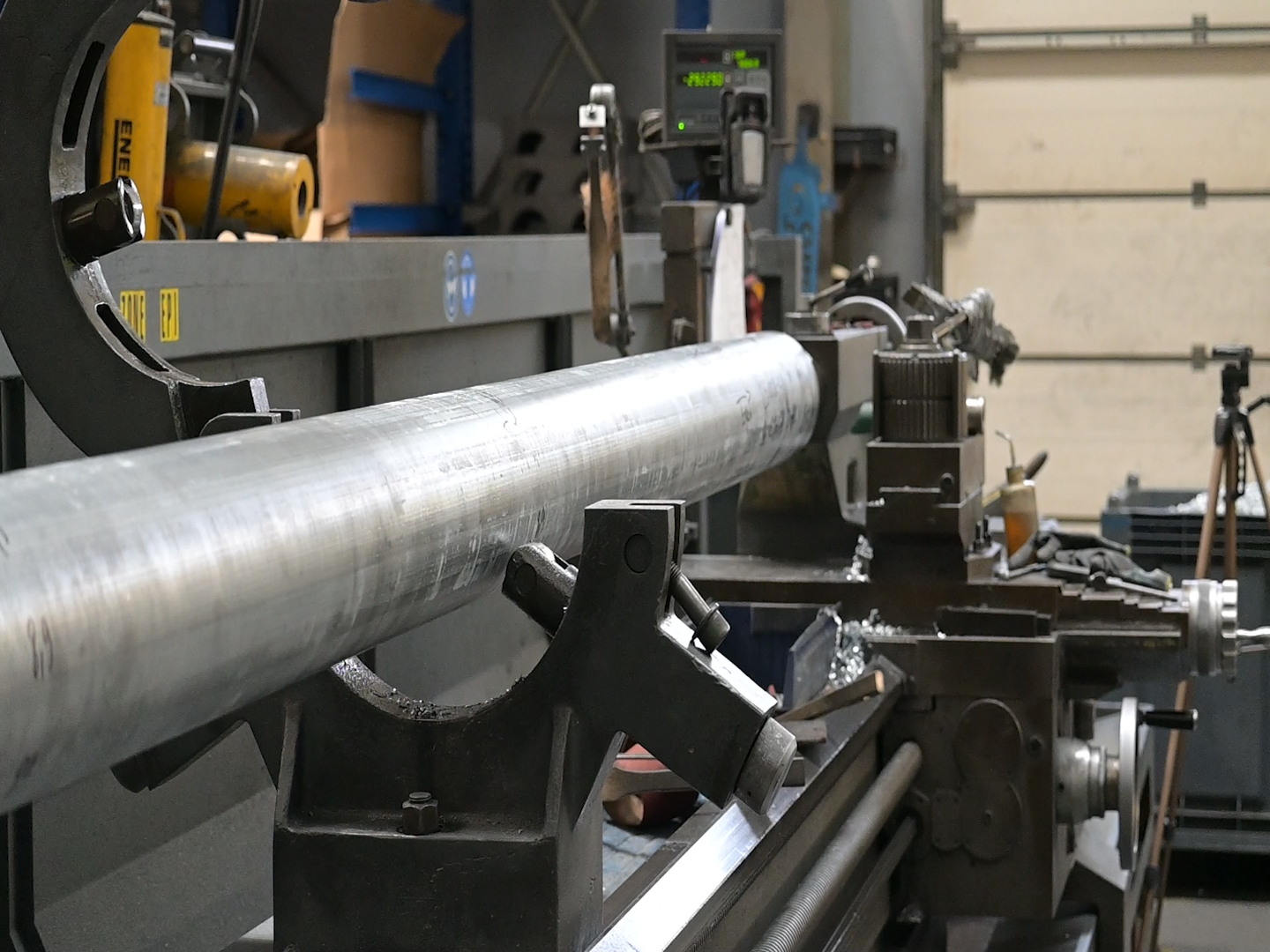 Metal rod on a machine in a workshop, with various tools and equipment in the background.
