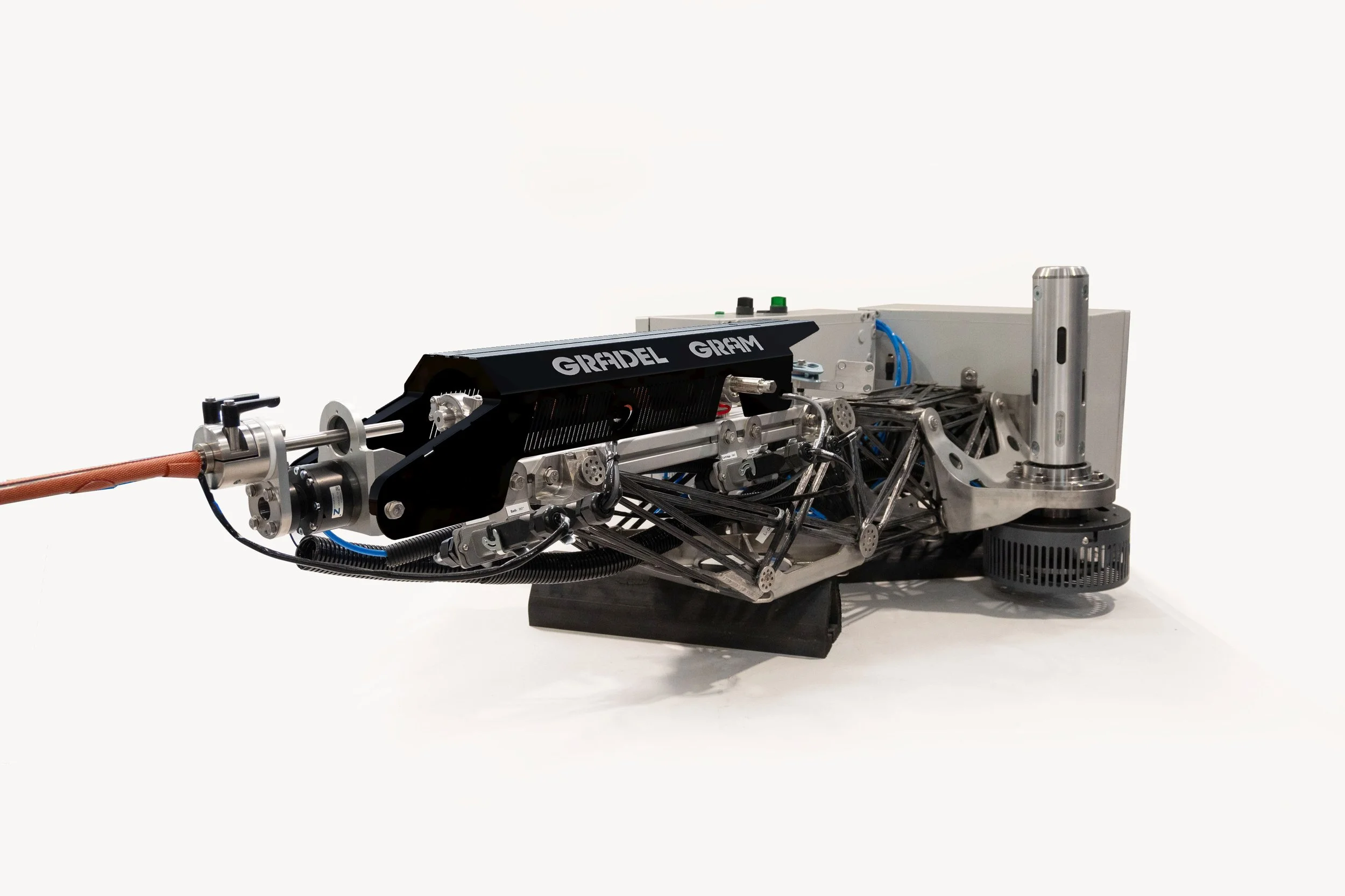 A robotic arm with a black component labeled Graidel GRAIM, metallic framework, wiring, and a copper pipe extending from the left, set against a plain white background.