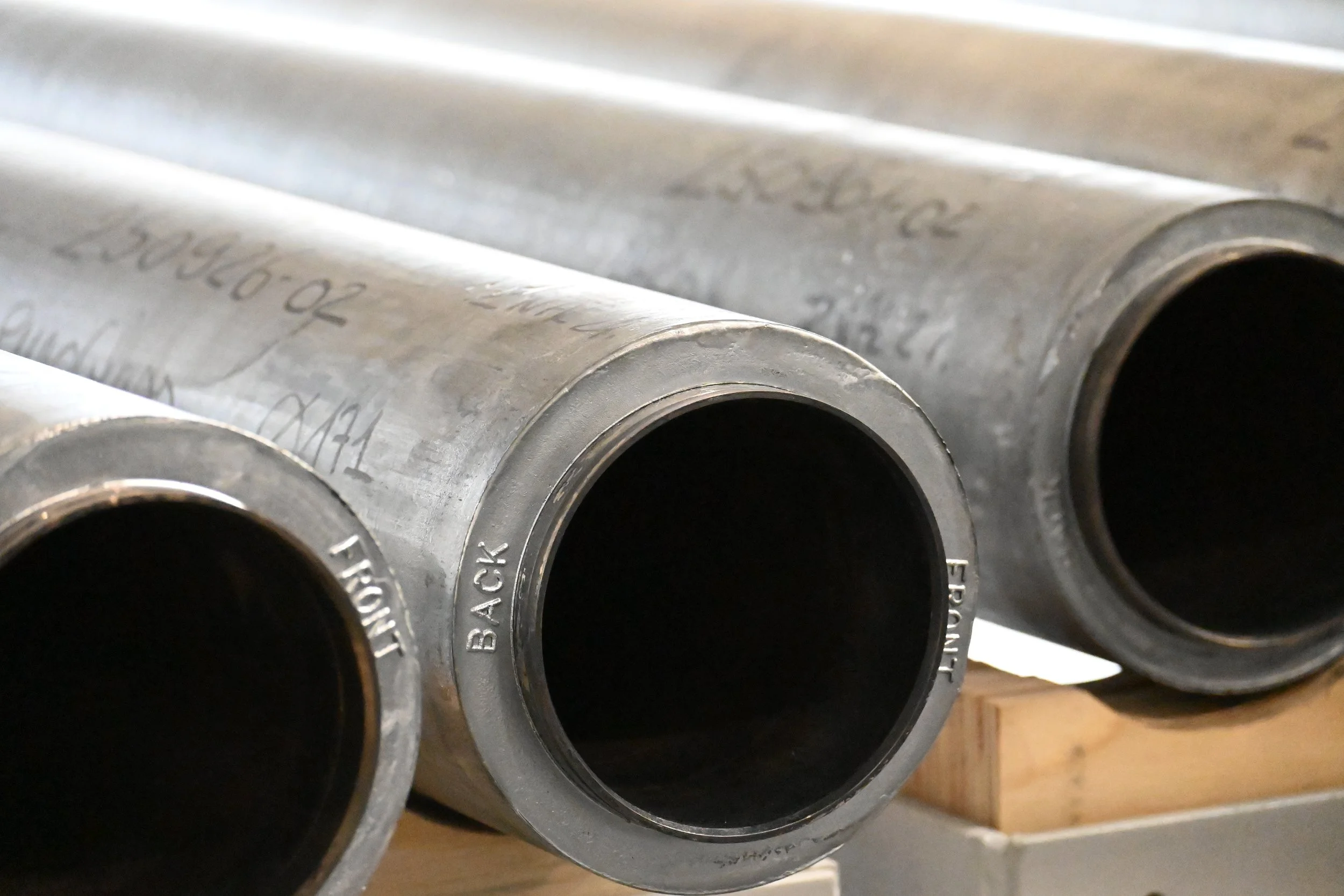 Close-up of three large metallic pipes with engraved text, resting on a wooden support.