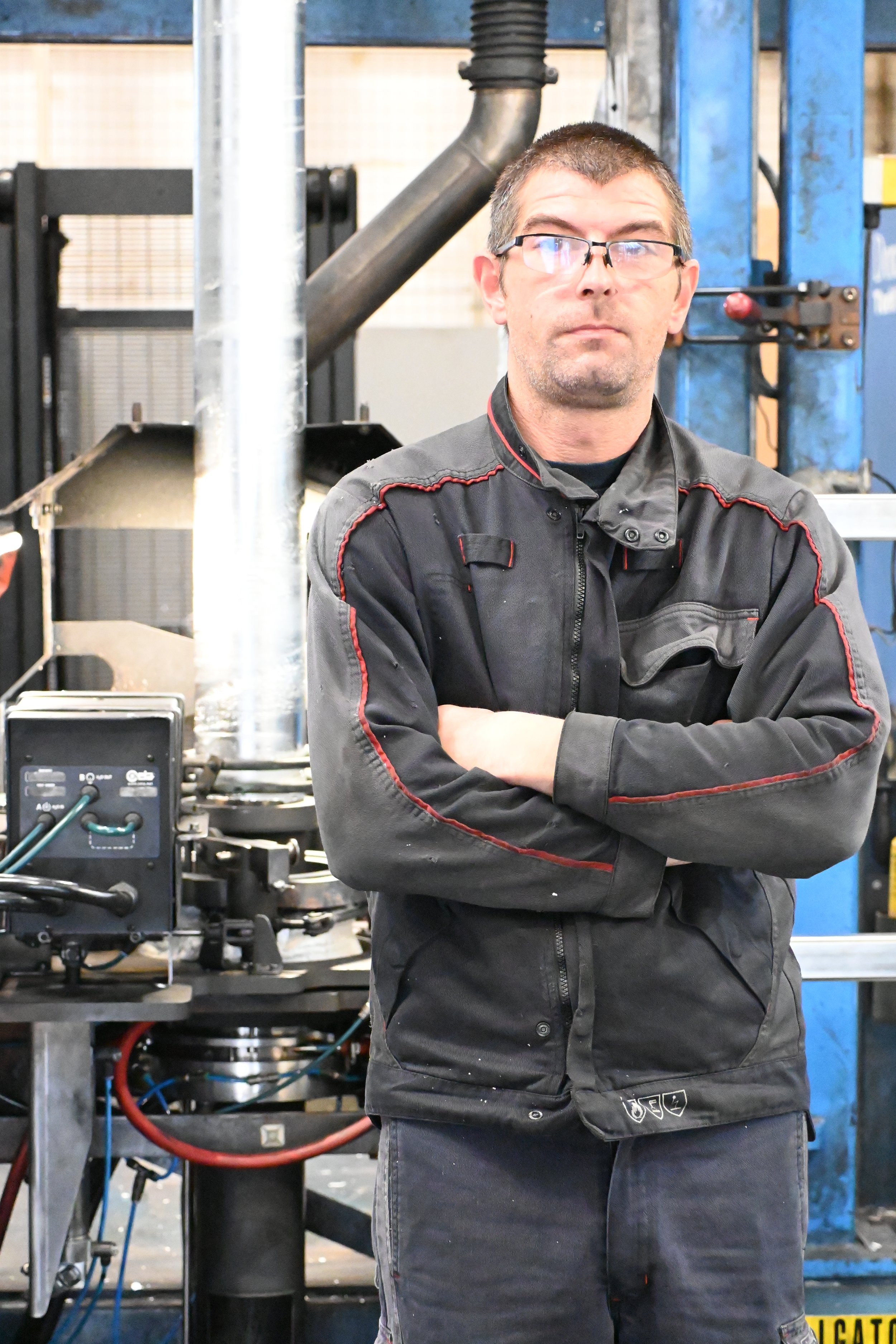 A man with a beard wearing a navy blue Gradel sweatshirt standing in front of industrial equipment in a manufacturing or processing facility.