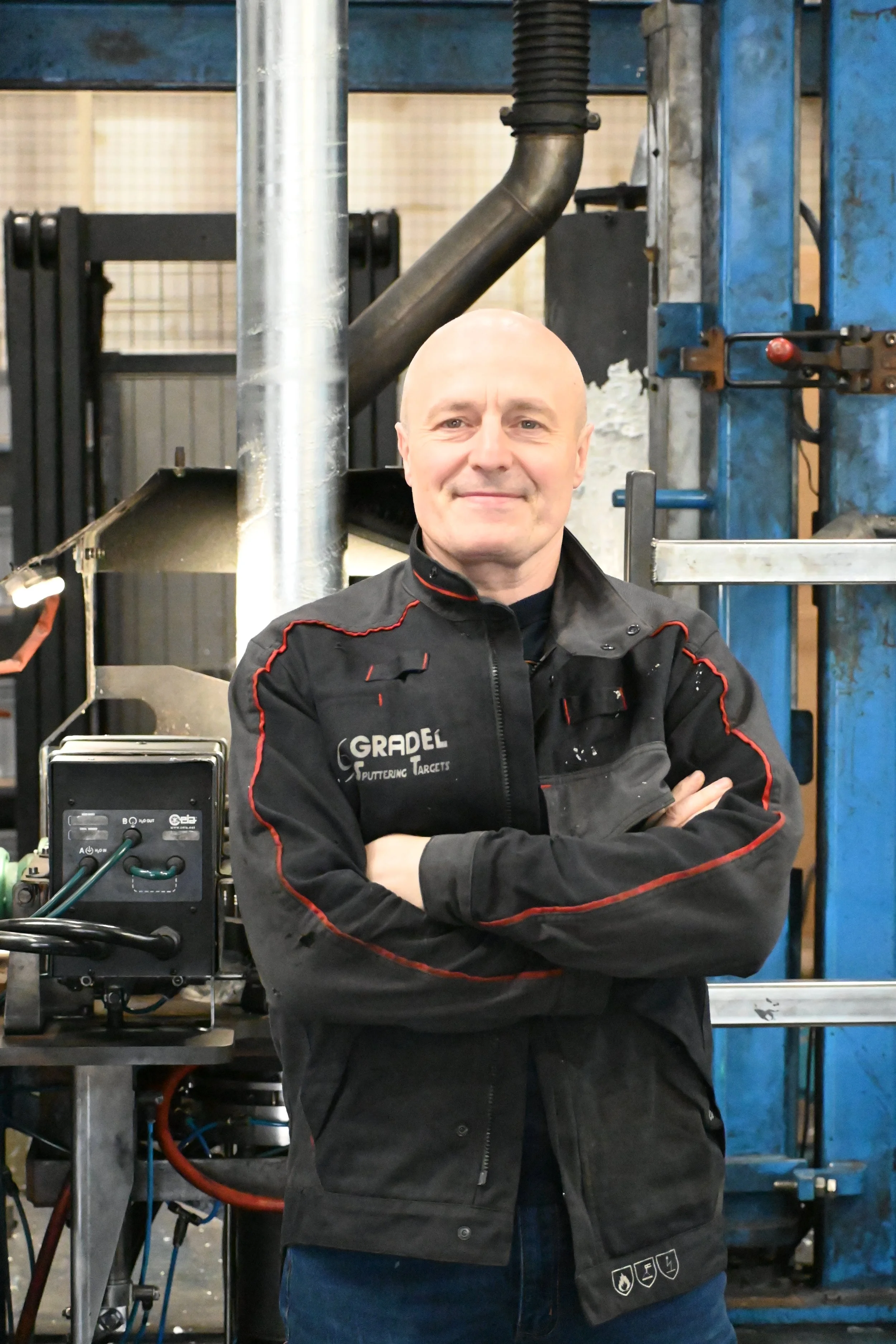 A smiling man in a blue Gradel sweatshirt standing in front of industrial machinery in a factory setting.