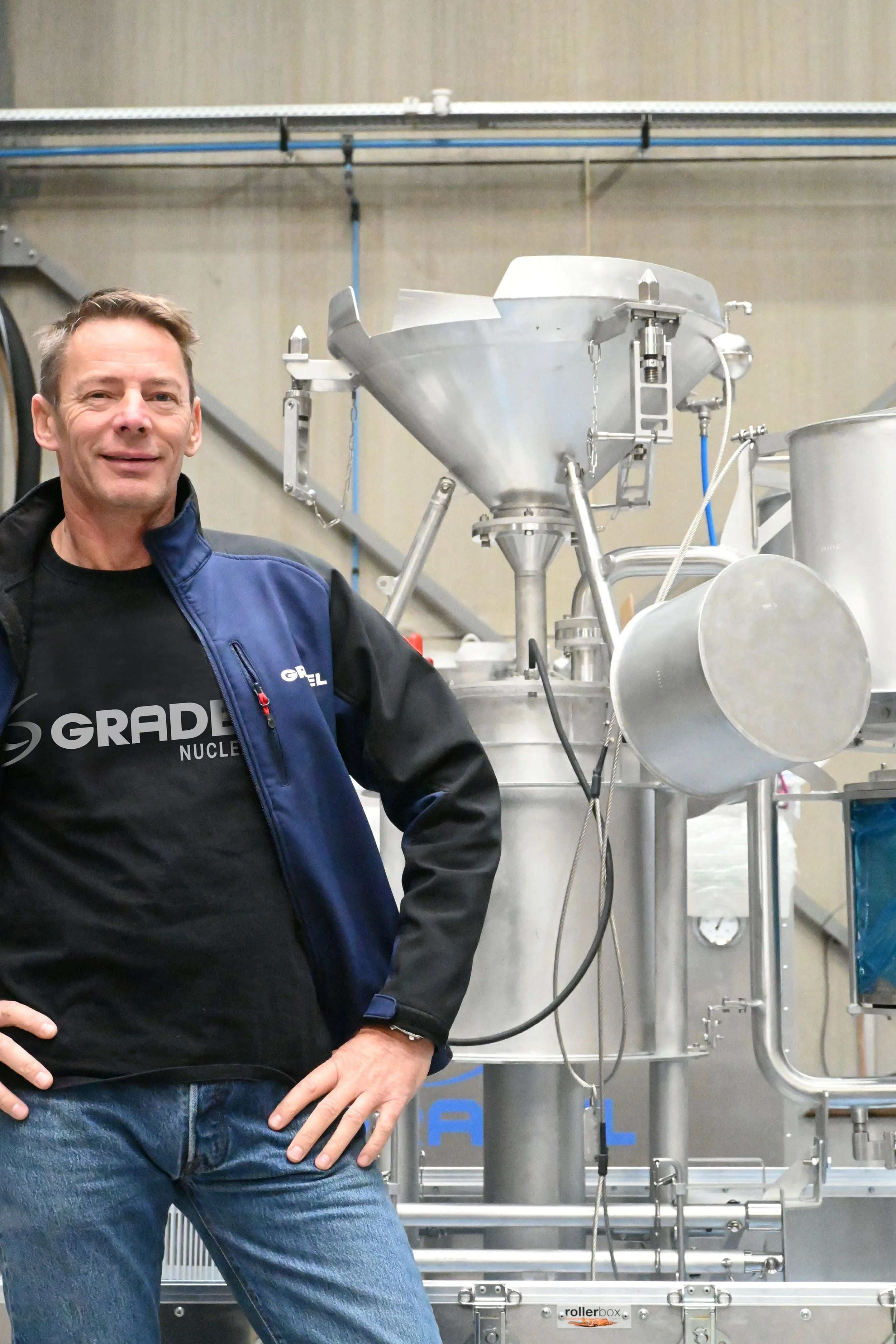 Marc NONNENMACHER in a navy Blue Gradel branded jacket standing in a manufacturing or industrial setting with stainless steel machinery behind him.