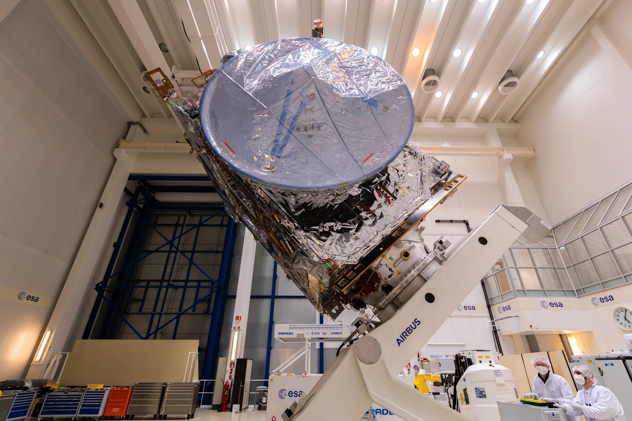 Laboratory with scientific equipment and two scientists in protective gear examining a satellite module.