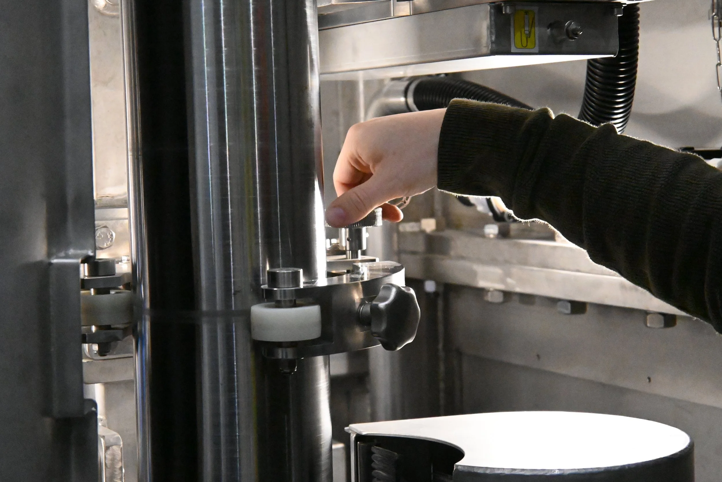 A person adjusting a part of a stainless steel industrial machine, possibly in a manufacturing or laboratory setting.