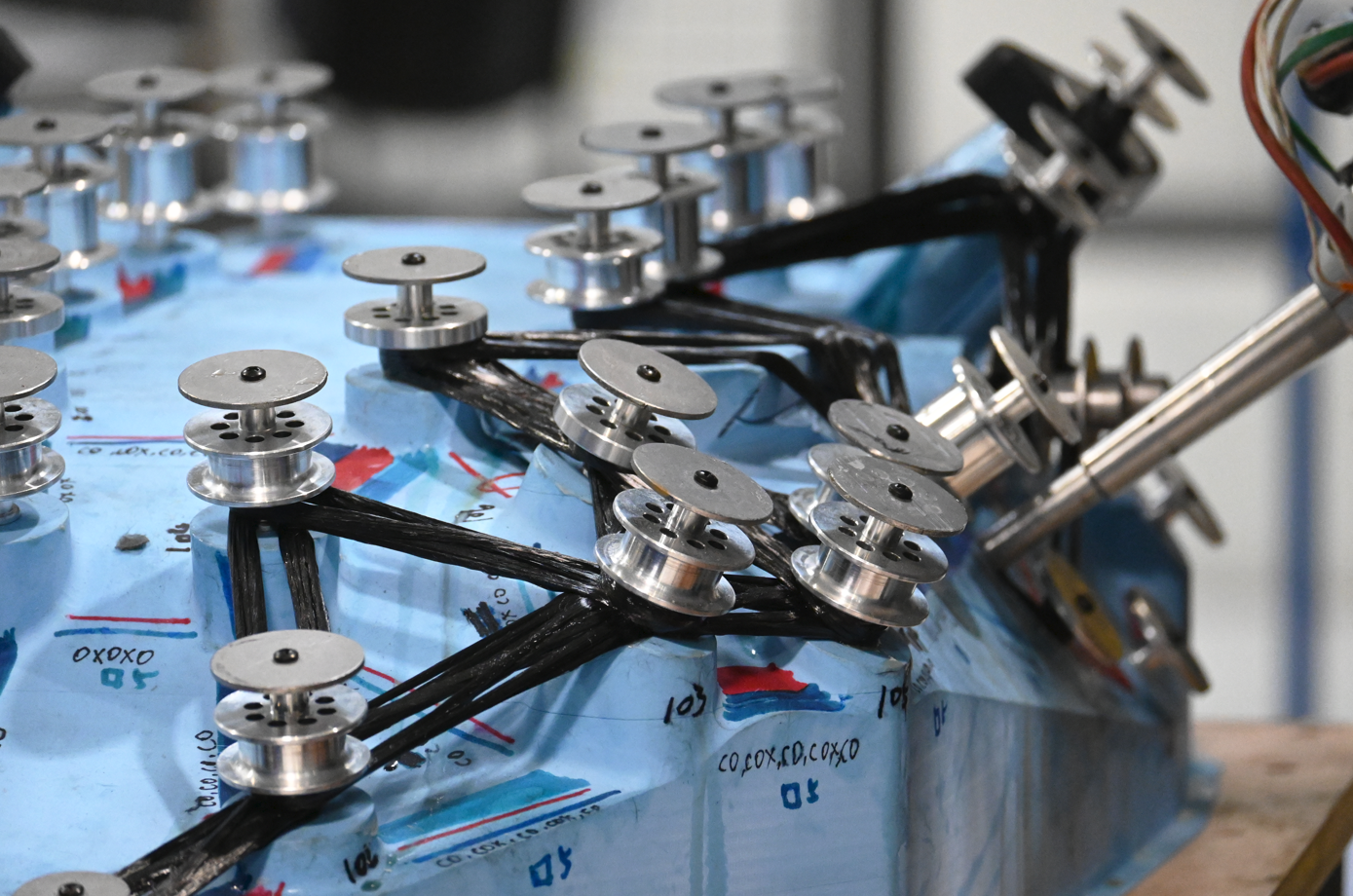 Close-up of electronic components with multiple small metal wheels connected by black wires on a blue surface.