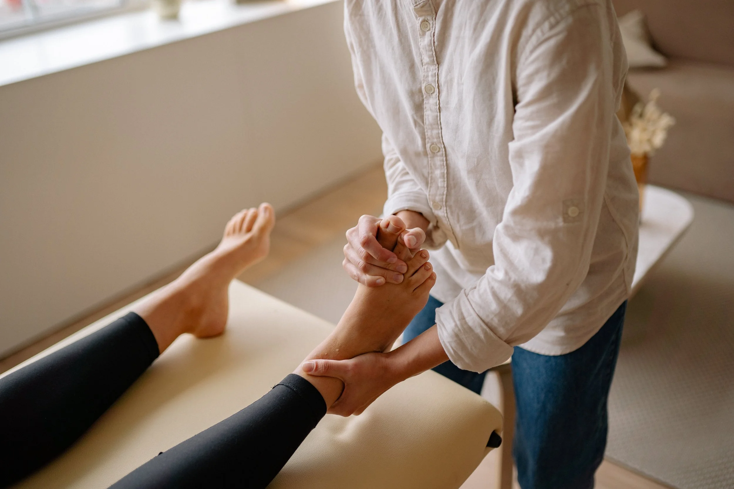 A physical therapist holds a patient's foot and ankle during a therapy session in a clinic.