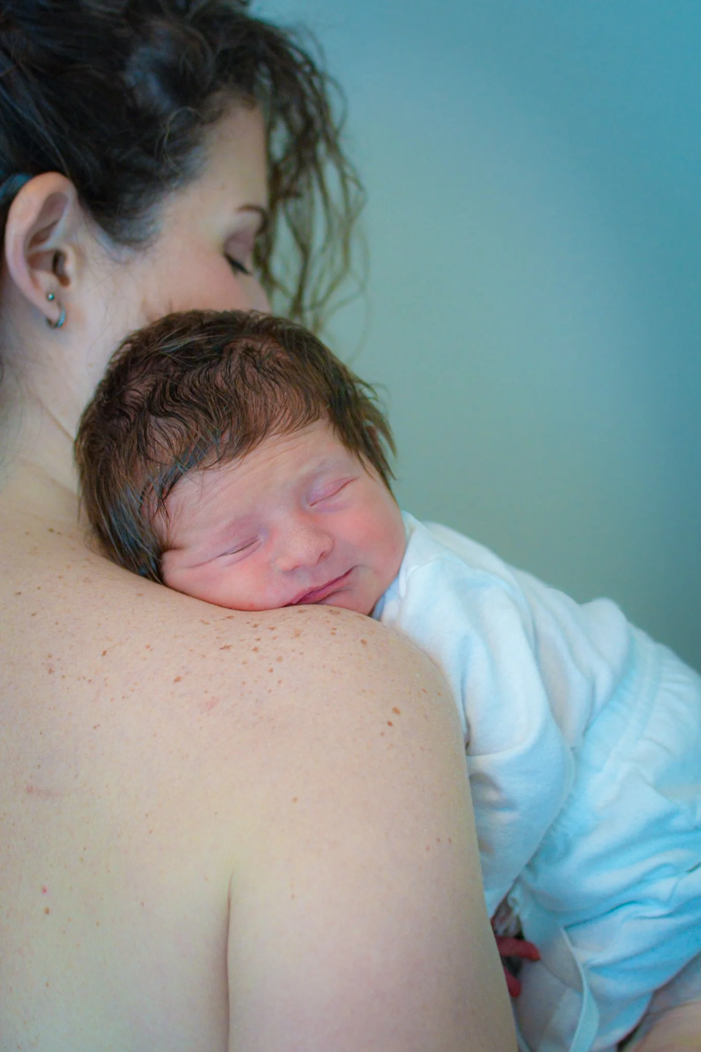 A woman holding a sleeping newborn baby on her shoulder, with the baby's face resting on her shoulder.